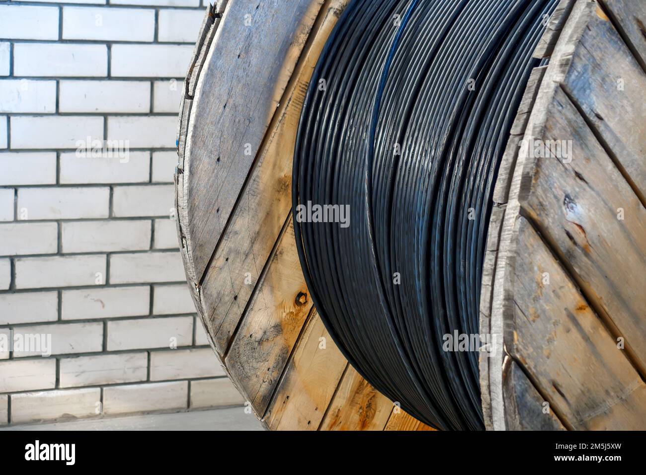 Il nuovo cavo di alimentazione nero è avvolto su una bobina di legno. Sfondo. Cavo per posa sotterranea. Foto Stock