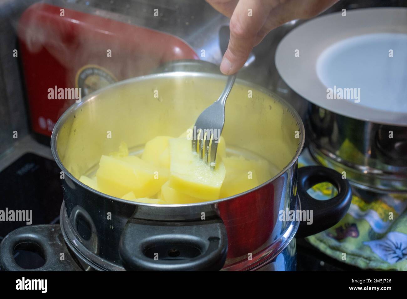 Patate in pentola tipo vaporiera che vengono forked per vedere se sono cotte completamente. Foto Stock