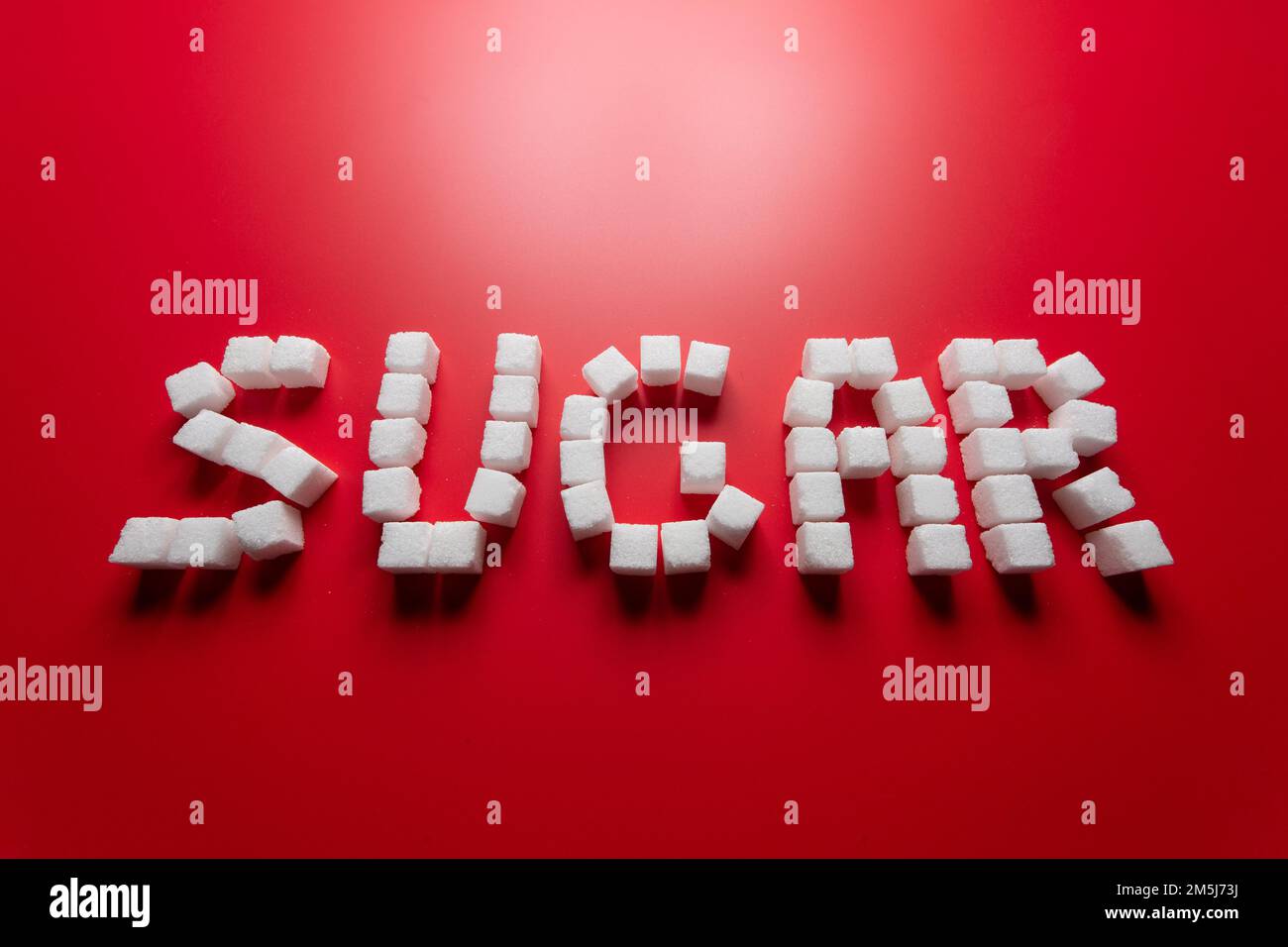 la parola zucchero è composta da cubetti di zucchero su sfondo rosso. foto sul tema dei pericoli del consumo di zucchero raffinato Foto Stock