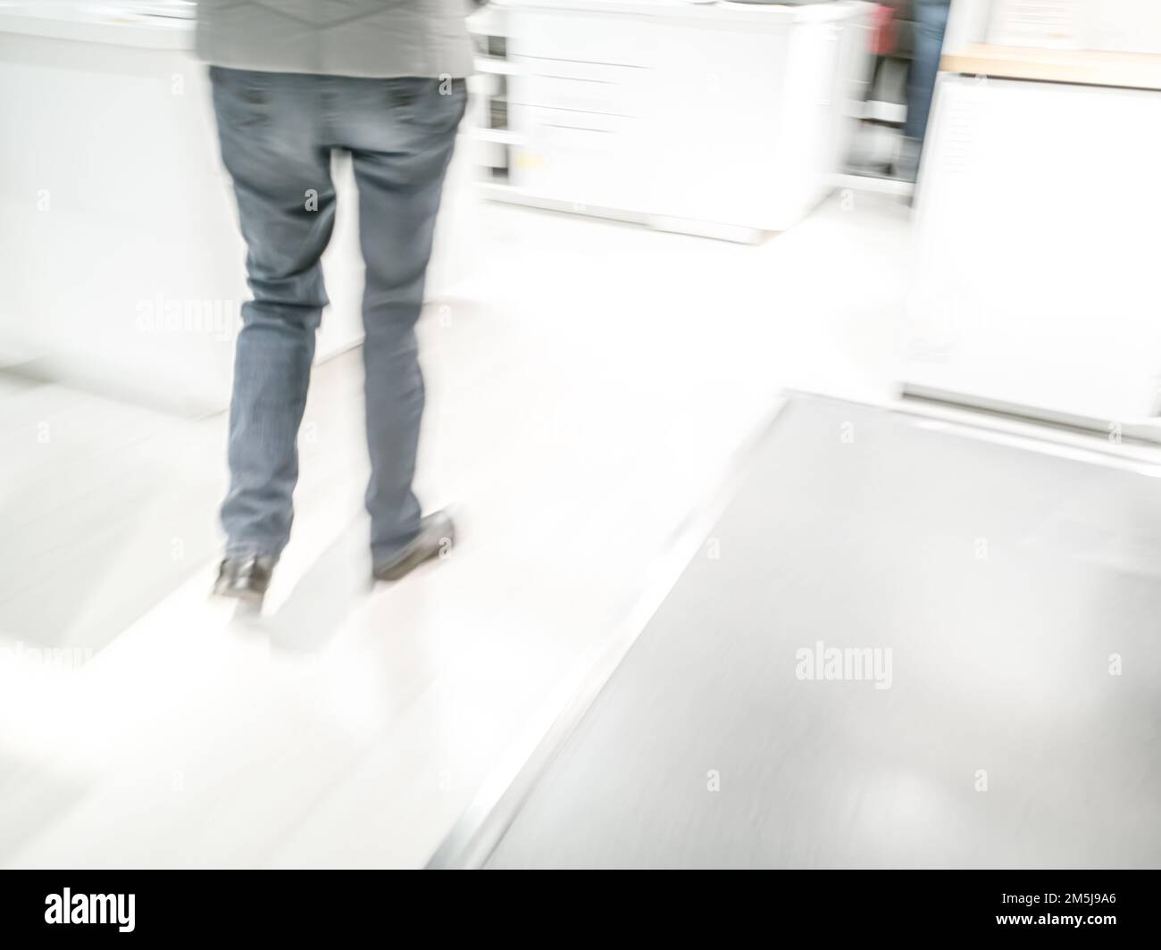 Gambe e piedi di una persona vista da dietro camminando in un negozio - sfocatura del movimento, chiave alta Foto Stock