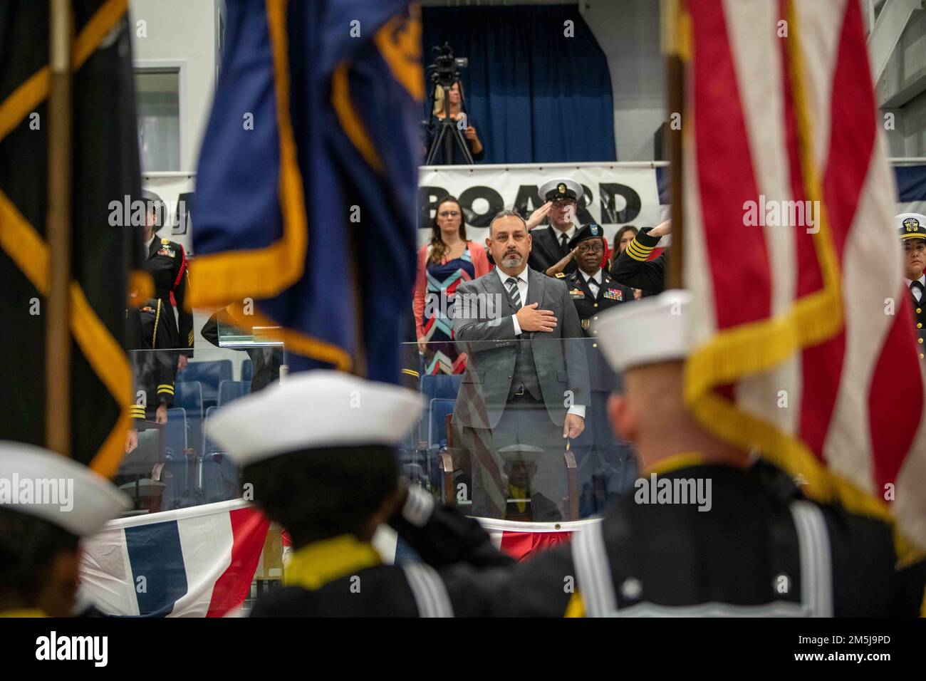 L'onorevole Gilbert R. Cisneros, Sottosegretario alla Difesa per il personale e la preparazione, pone la mano sul suo cuore durante l'inno nazionale nella Midway Ceremonial Drill Hall durante una cerimonia di laurea pass-in-review al Recruit Training Command. Più di 40.000 reclute ogni anno si allenano presso l'unico campo di stivali della Marina. Foto Stock