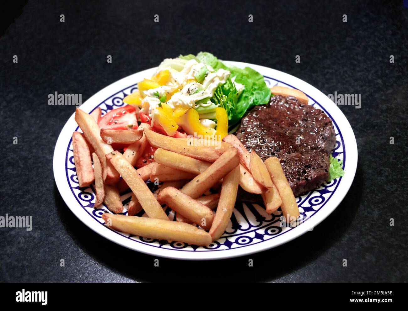 vista dall'alto di bistecche, patatine, insalata e maionese su un piatto di ceramica decorato, fotografia di cibo in studio Foto Stock