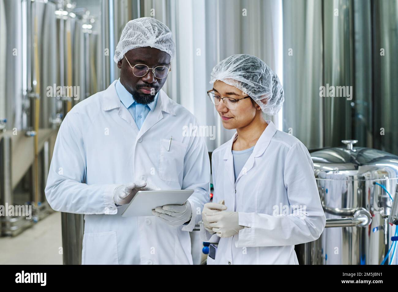 Coppia multietnica di ingegneri che lavorano insieme al tablet digitale mentre lavorano in birreria Foto Stock