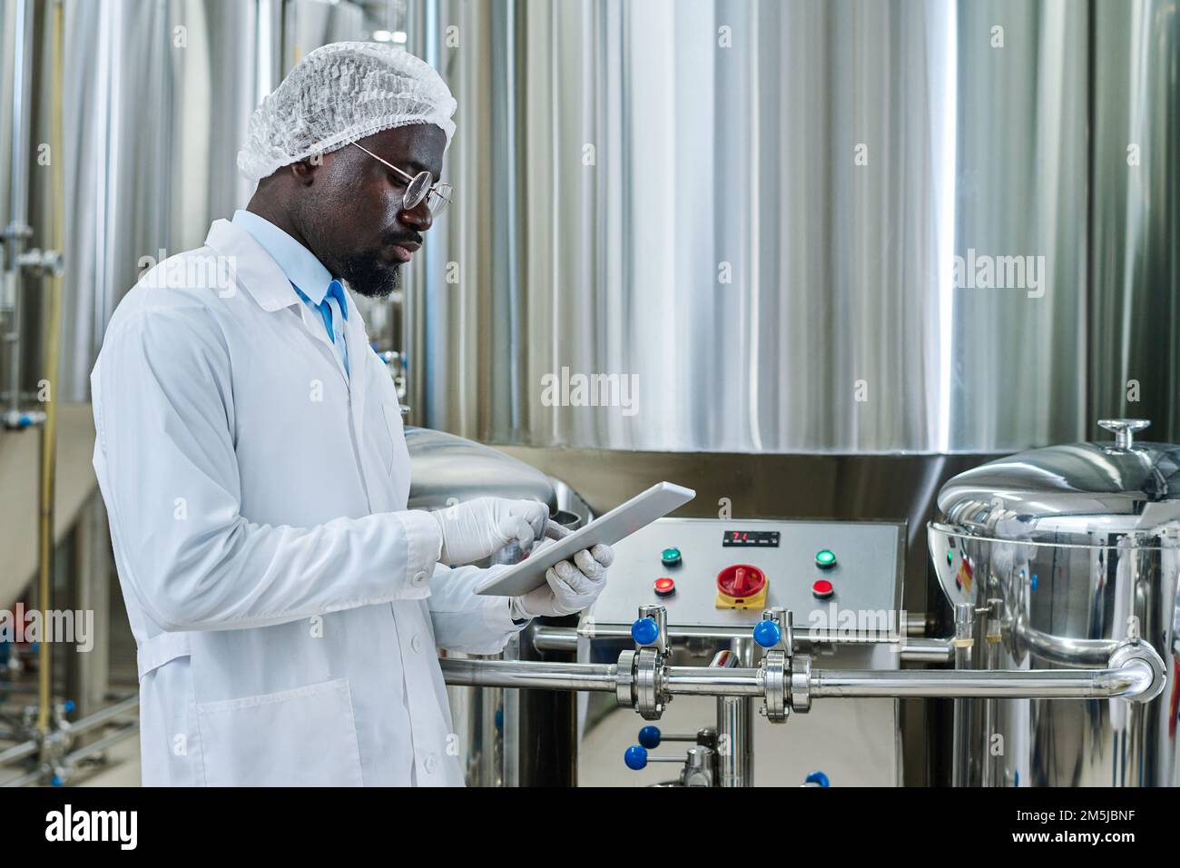 Ingegnere professionista in camice bianco davanti alle apparecchiature e che lavora online su un tablet pc Foto Stock