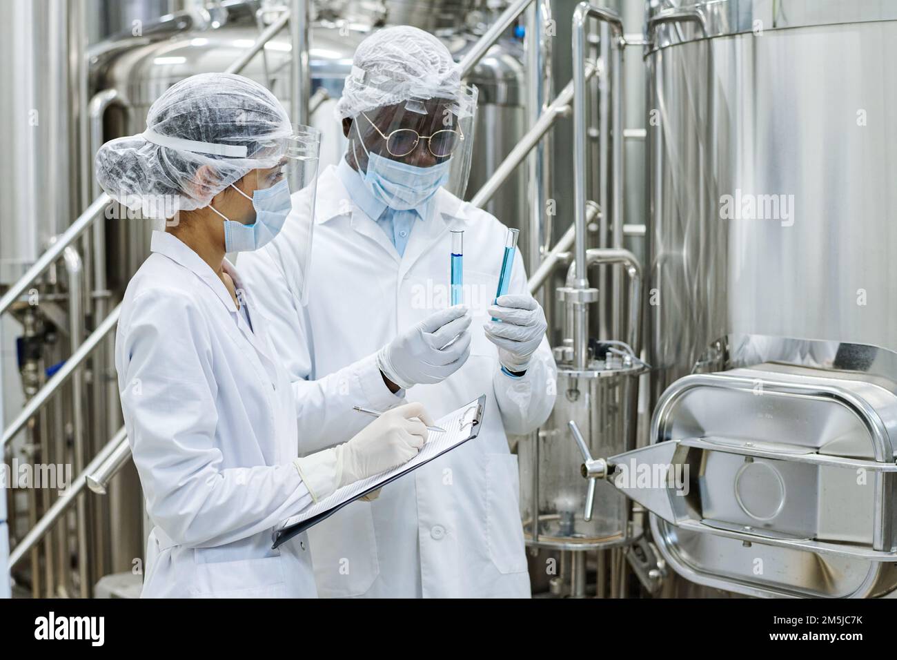 Scienziato afro-americano che esamina il liquido nelle provette mentre il suo assistente prende appunti nel documento durante l'esperimento scientifico Foto Stock