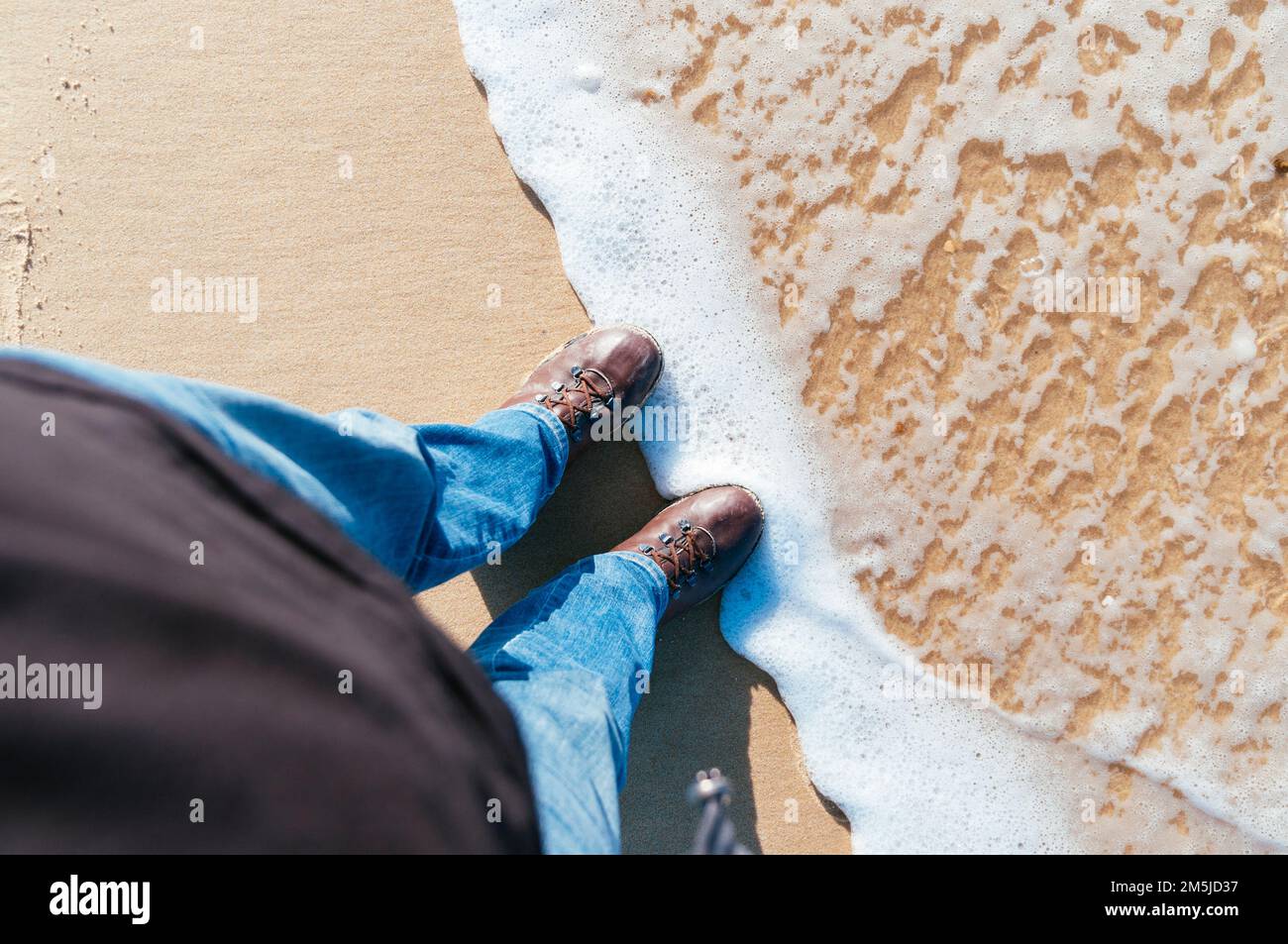 Uomo in jeans e stivali in piedi in una spiaggia in Francia nel mese di dicembre guardando verso il basso Foto Stock