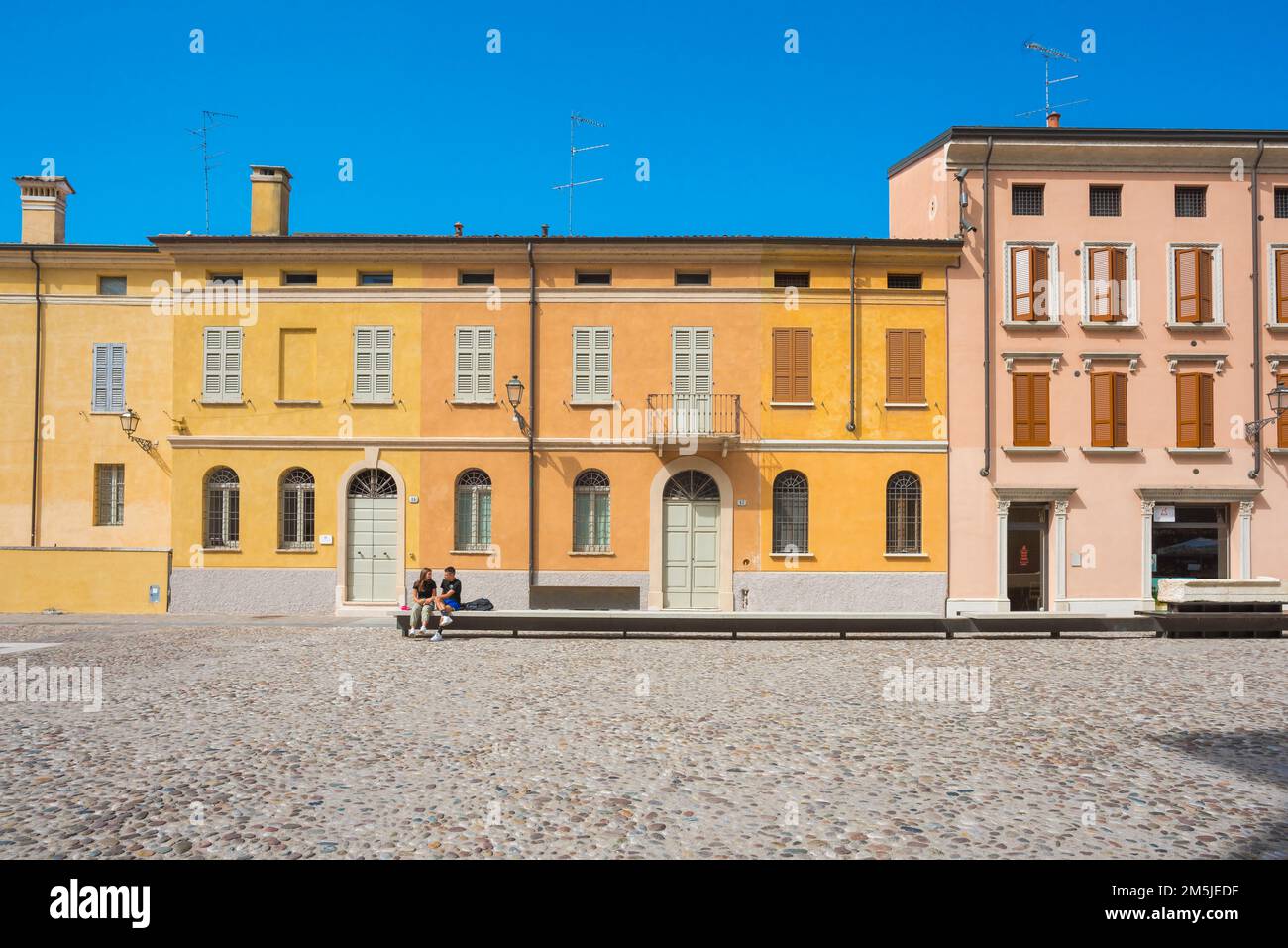 I giovani amano l'estate in Europa, vista di due giovani che parlano seduti soli in una colorata piazza di Mantova, Lombardia, Italia Foto Stock