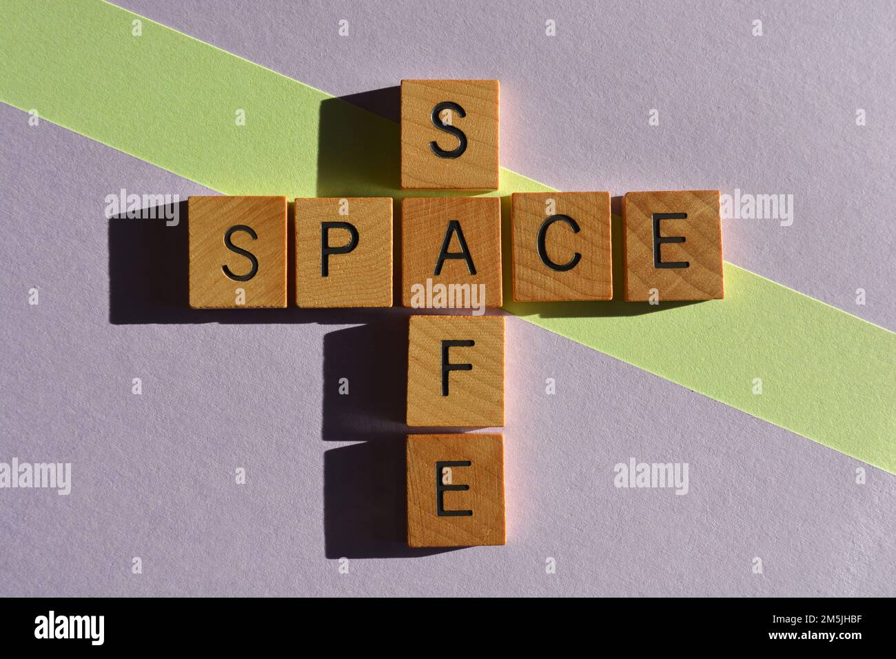 Safe Space, parole in lettere alfabetiche di legno a forma di croce isolate su sfondo verde e viola Foto Stock