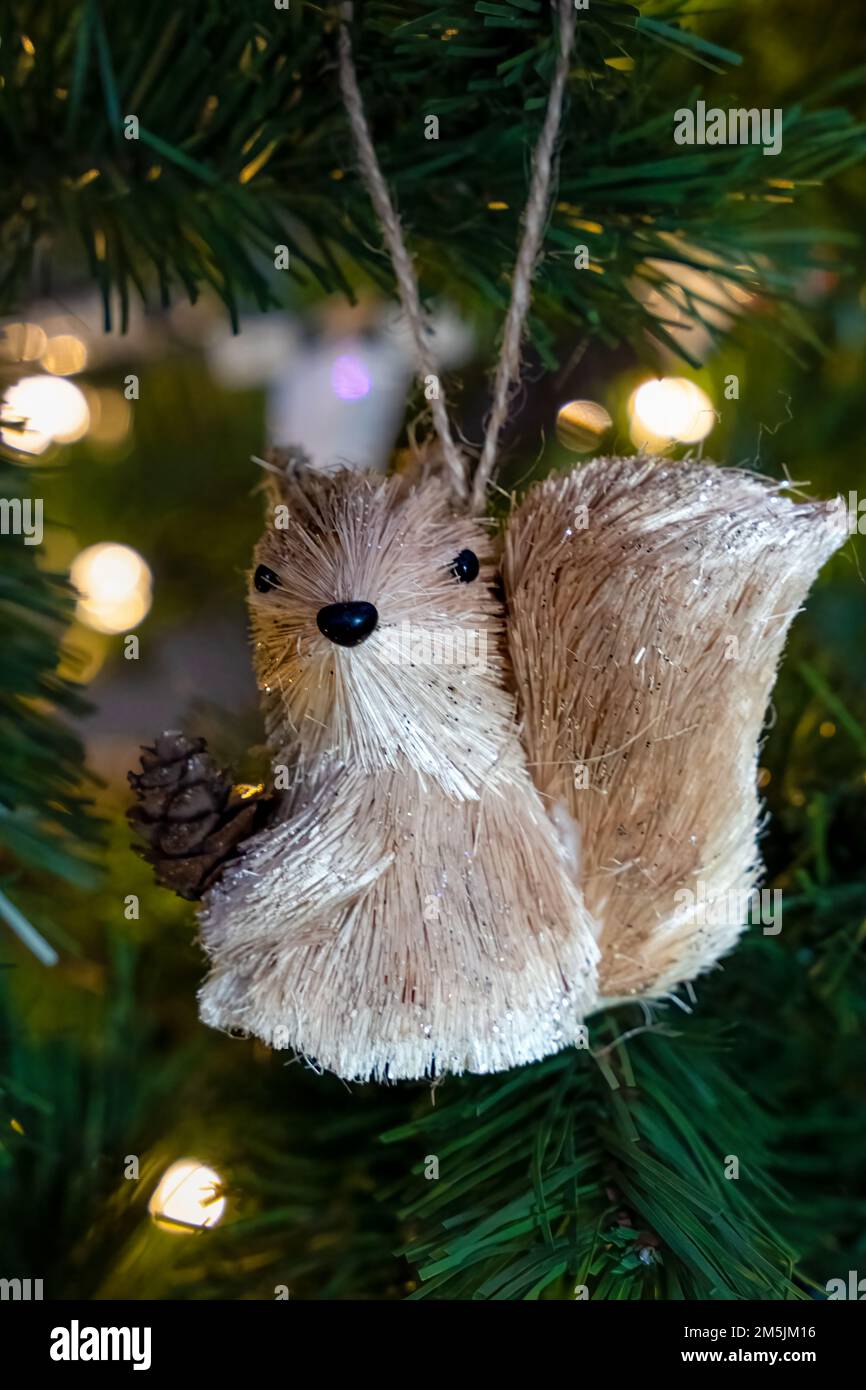 Ornamento di Natale scoiattolo seduto in un albero di Natale artificiale con luci di Natale sullo sfondo Foto Stock