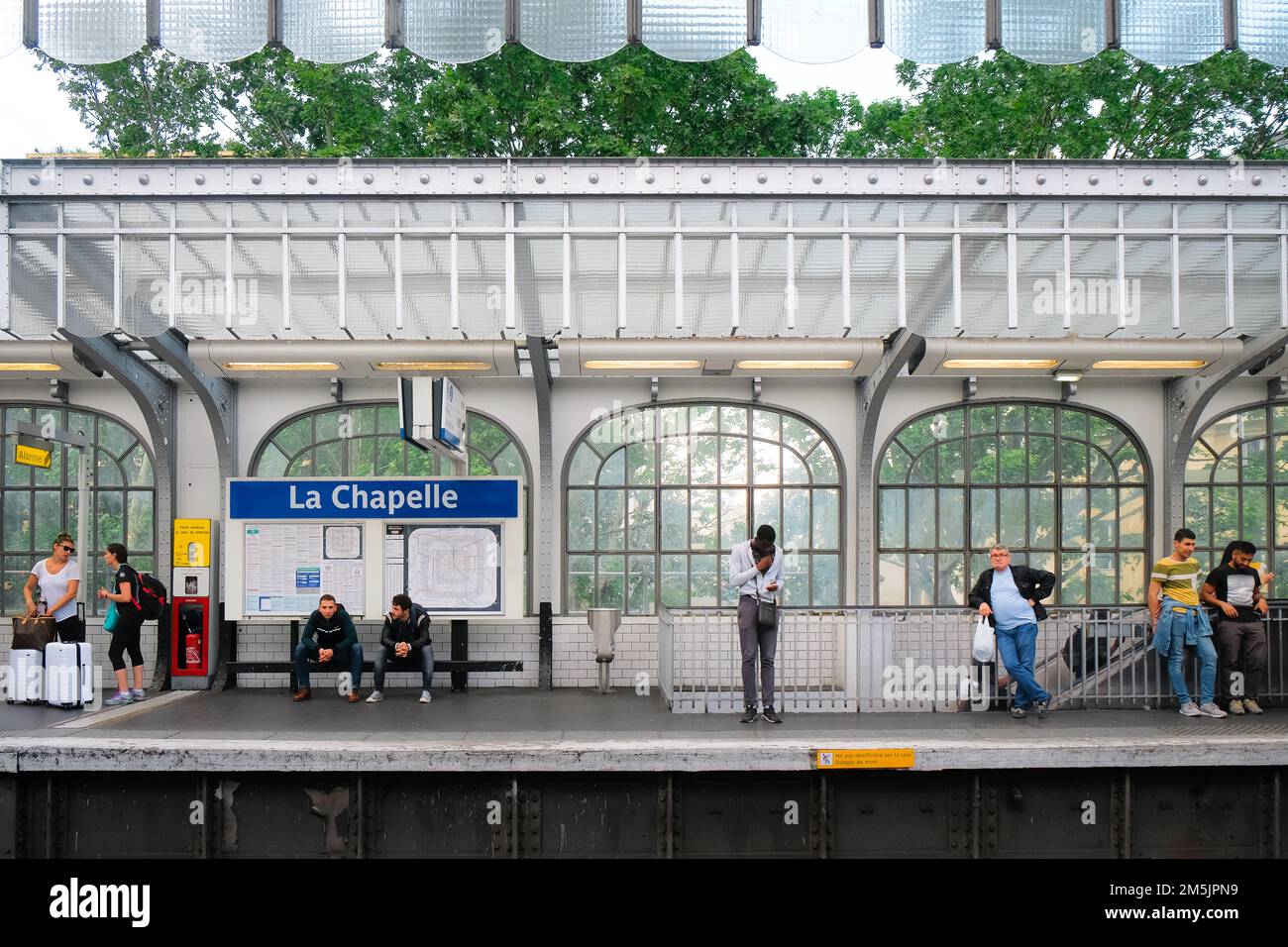 Parigi, Francia - la gente aspetta il prossimo treno all'interno della stazione della metropolitana la Chapelle. Pendolari in attesa sulla piattaforma. Interni in vetro trasparente colorato. Foto Stock