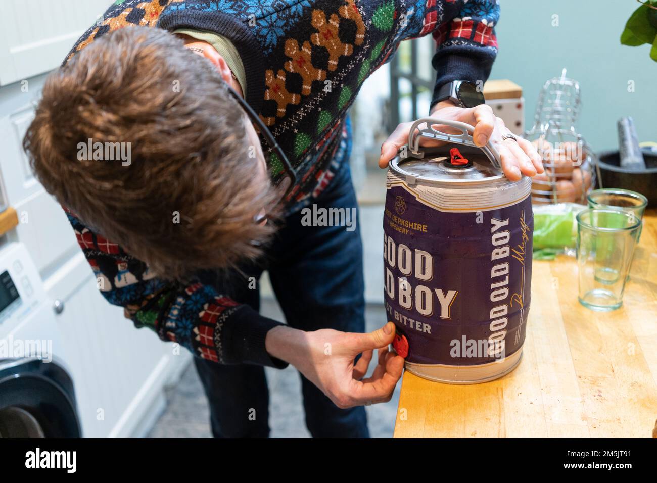 Un uomo a casa con un ponticello di Natale che apre il rubinetto su un mini barile di buon vecchio ragazzo amaro per versare una birra a Natale, in Inghilterra Foto Stock