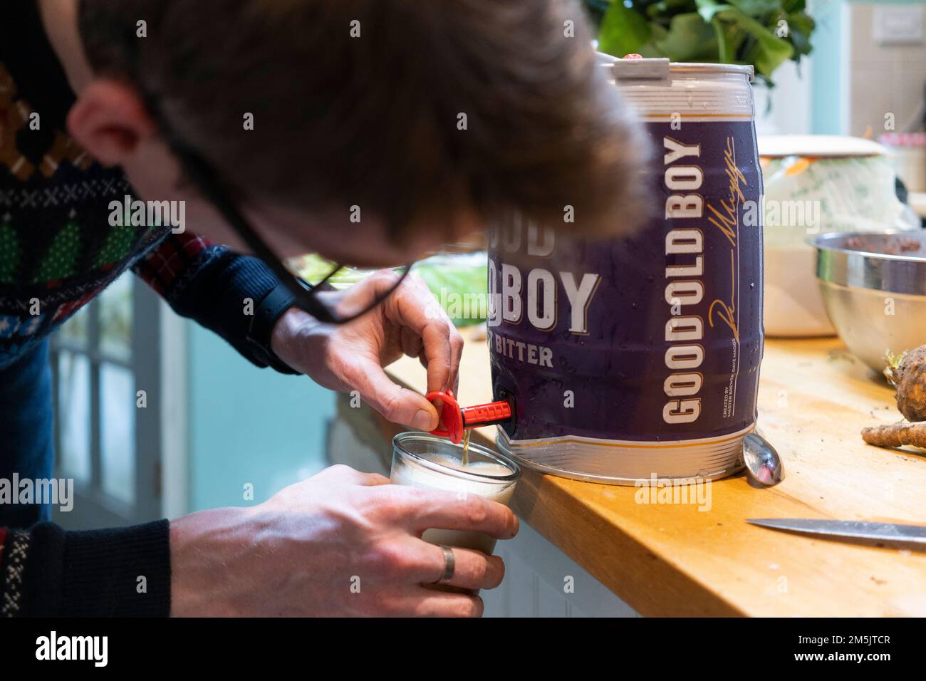 Un uomo a casa con un ponticello di Natale che apre il rubinetto su un mini barile di buon vecchio ragazzo amaro per versare una birra a Natale, in Inghilterra Foto Stock