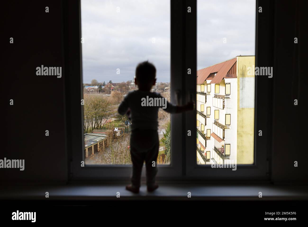 Bambino solitario in piedi sul davanzale. Situazione pericolosa, rischio di caduta dal finestrino. Foto Stock