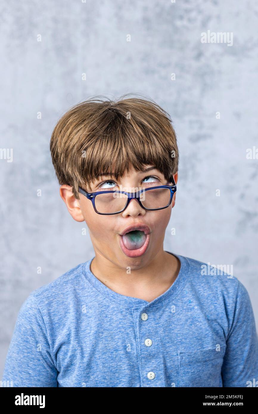 un ragazzino con gli occhiali che fanno un volto sciocco con una lingua blu che sporge e copia spazio Foto Stock