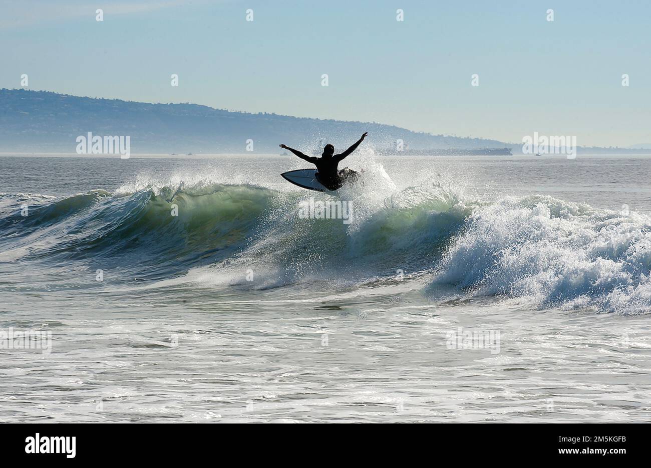 Surfista cavalcando un'onda a Venice Beach con la penisola di Palos Verdes sullo sfondo nella California meridionale. Foto Stock