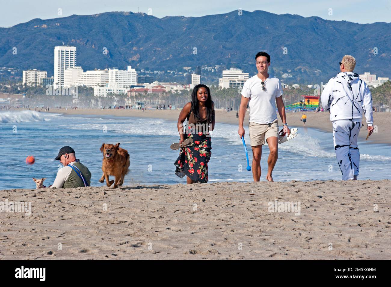Le persone che si godono una passeggiata a Venice Beach con il loro cane e lo skyline di Santa Monica sullo sfondo. Foto Stock