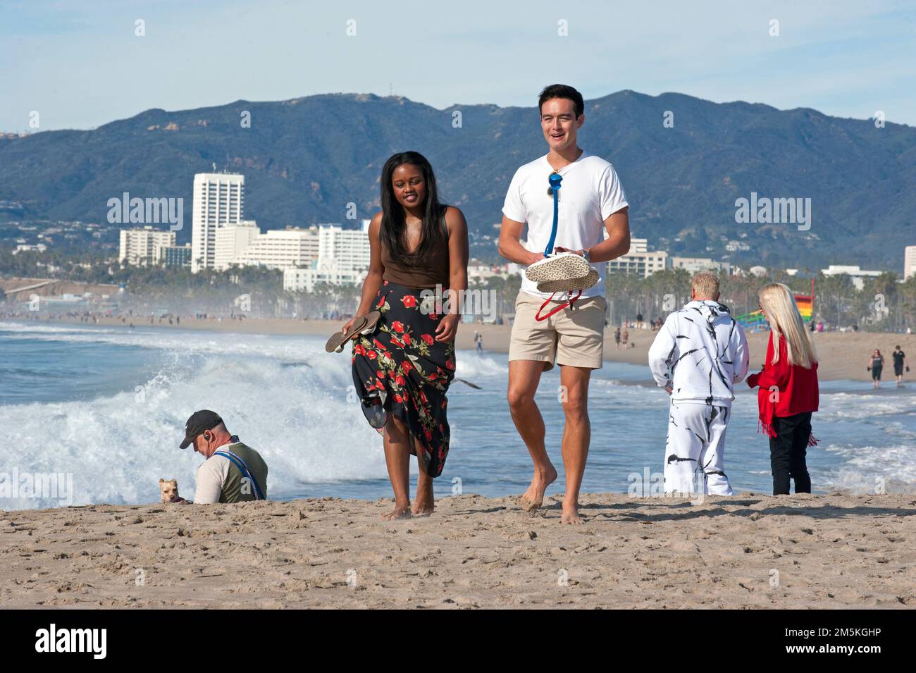 Le persone che si godono una passeggiata a Venice Beach con lo skyline di Santa Monica sullo sfondo. Foto Stock