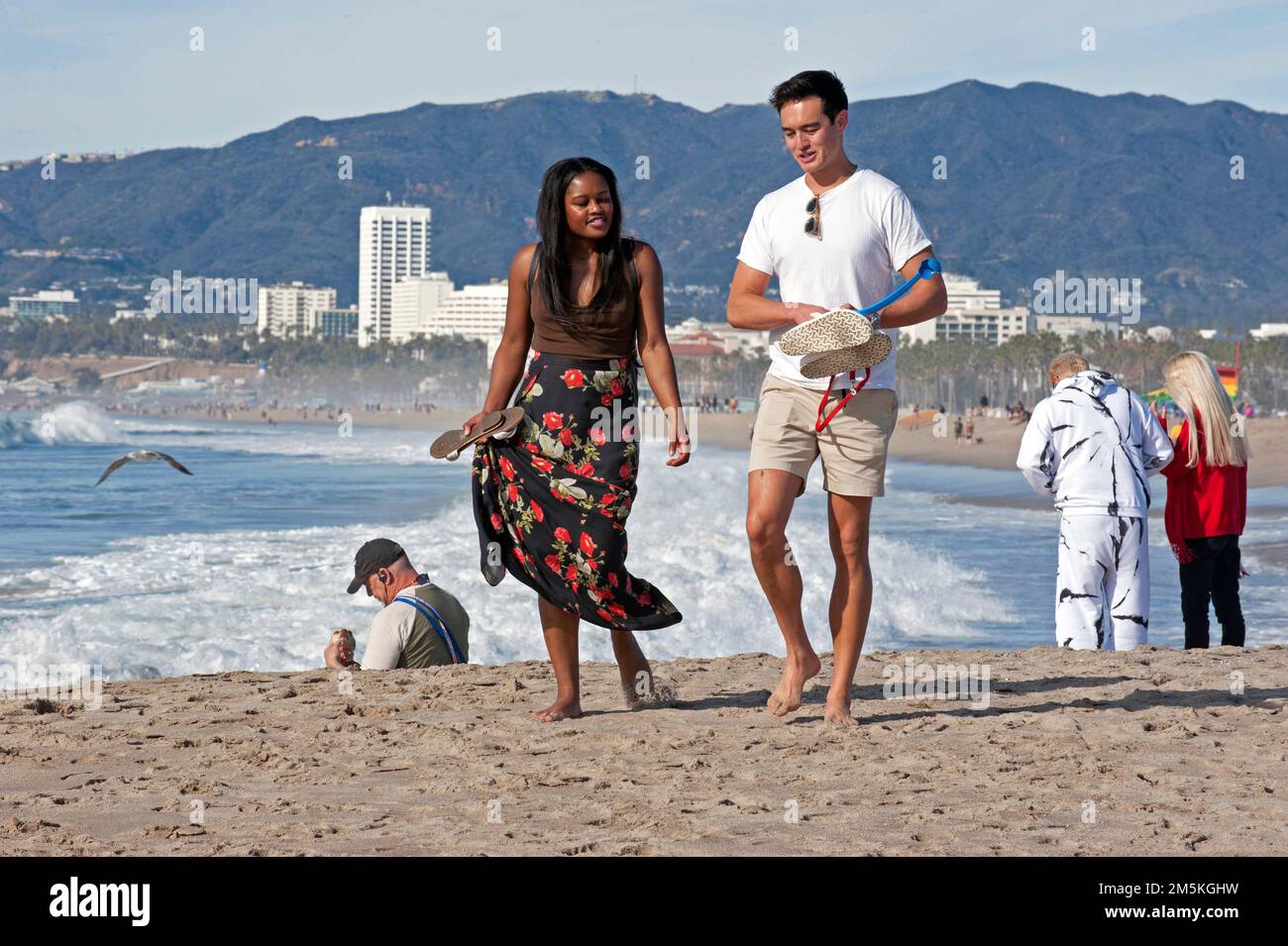 Le persone che si godono una passeggiata a Venice Beach con lo skyline di Santa Monica sullo sfondo. Foto Stock