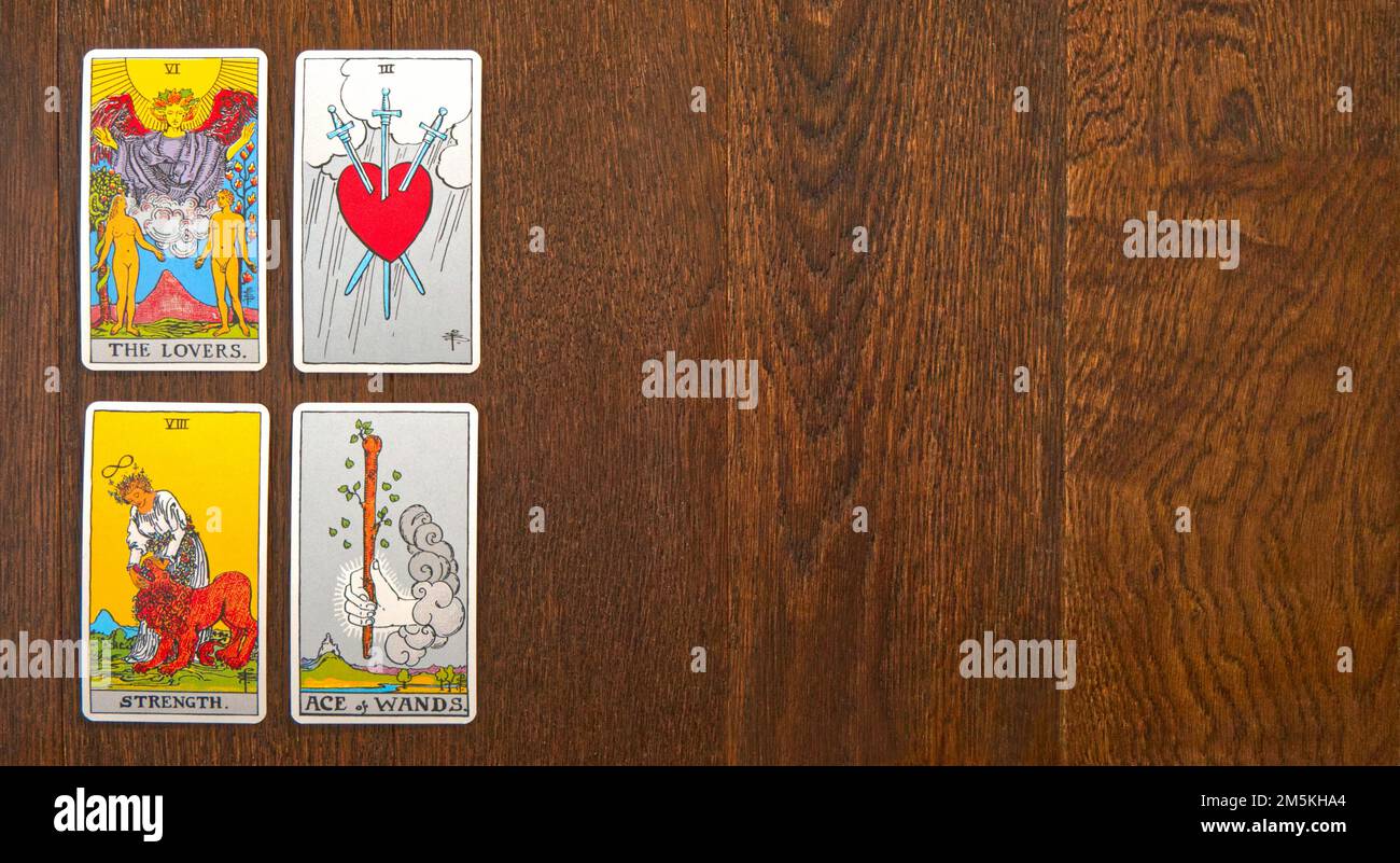Una diffusione di quattro carte Tarocchi Rider-Waite maggiore Arcana su un pavimento di legno; gli amanti, la forza, l'asso delle terre, tre di spade. Foto Stock