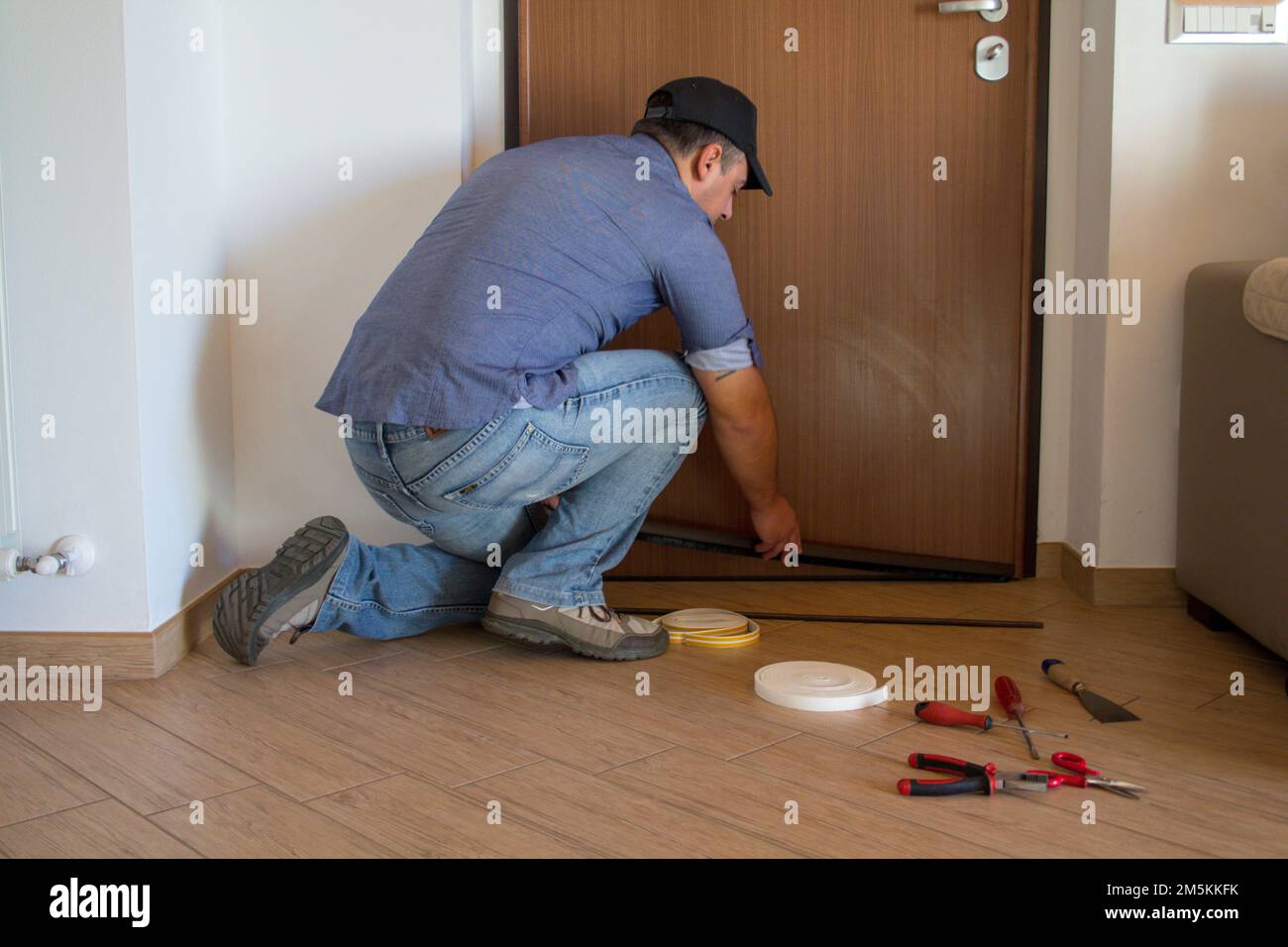 Immagine di un handyman che installa un dispositivo di esclusione della trazione sulla sua porta anteriore. Migliore isolamento termico e infiltrazione di aria fredda. Foto Stock