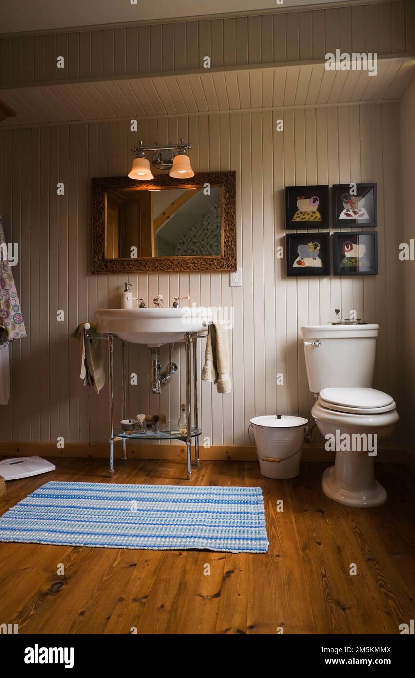 Lavello bianco su piedistallo cromato e WC con serbatoio alto nel bagno principale all'interno di un cottage in stile rustico di casa in legno. Foto Stock