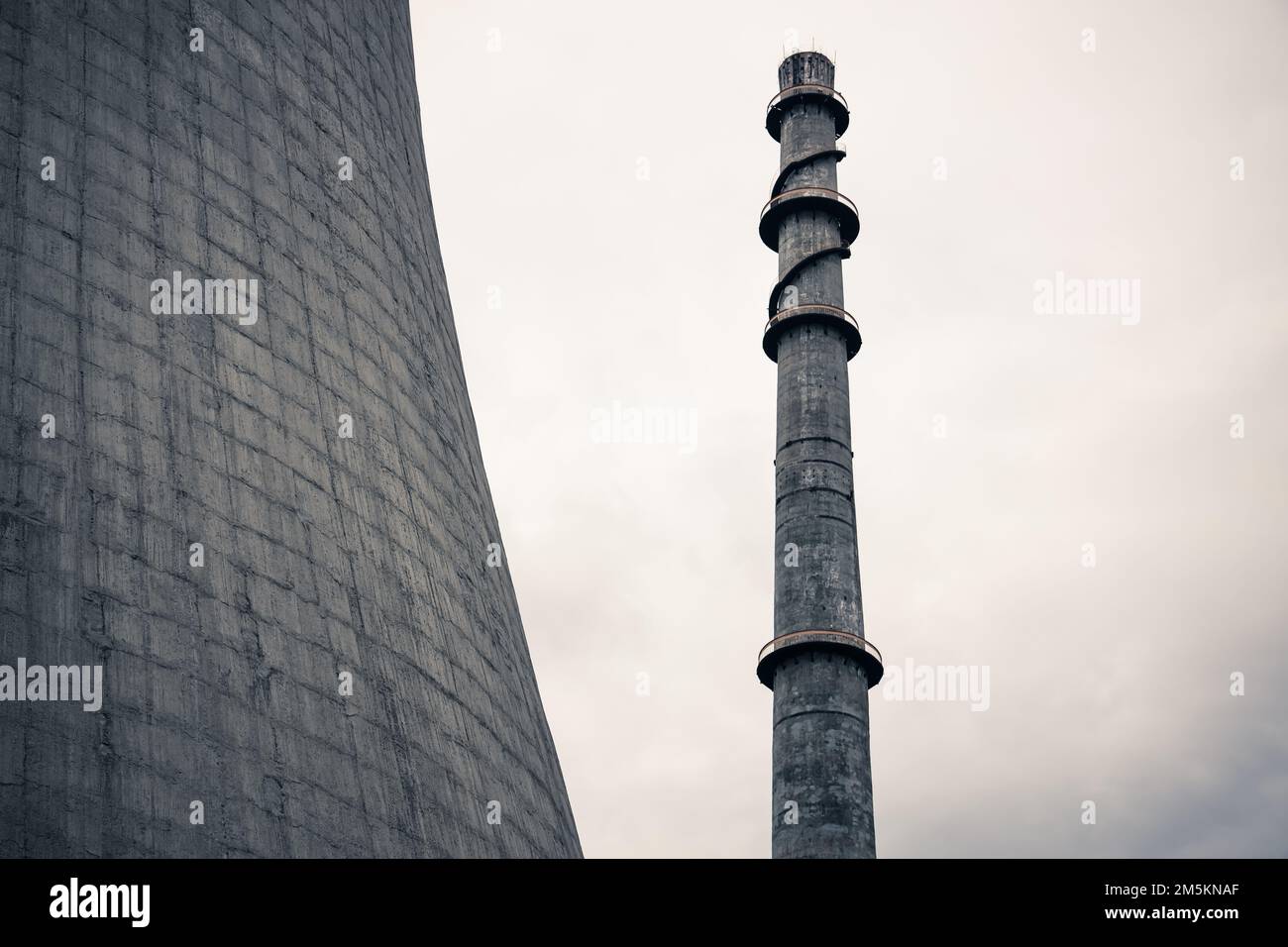 Un getto in scala di grigi a basso angolo di un camino a fumo accanto a una torre di raffreddamento del reattore Foto Stock