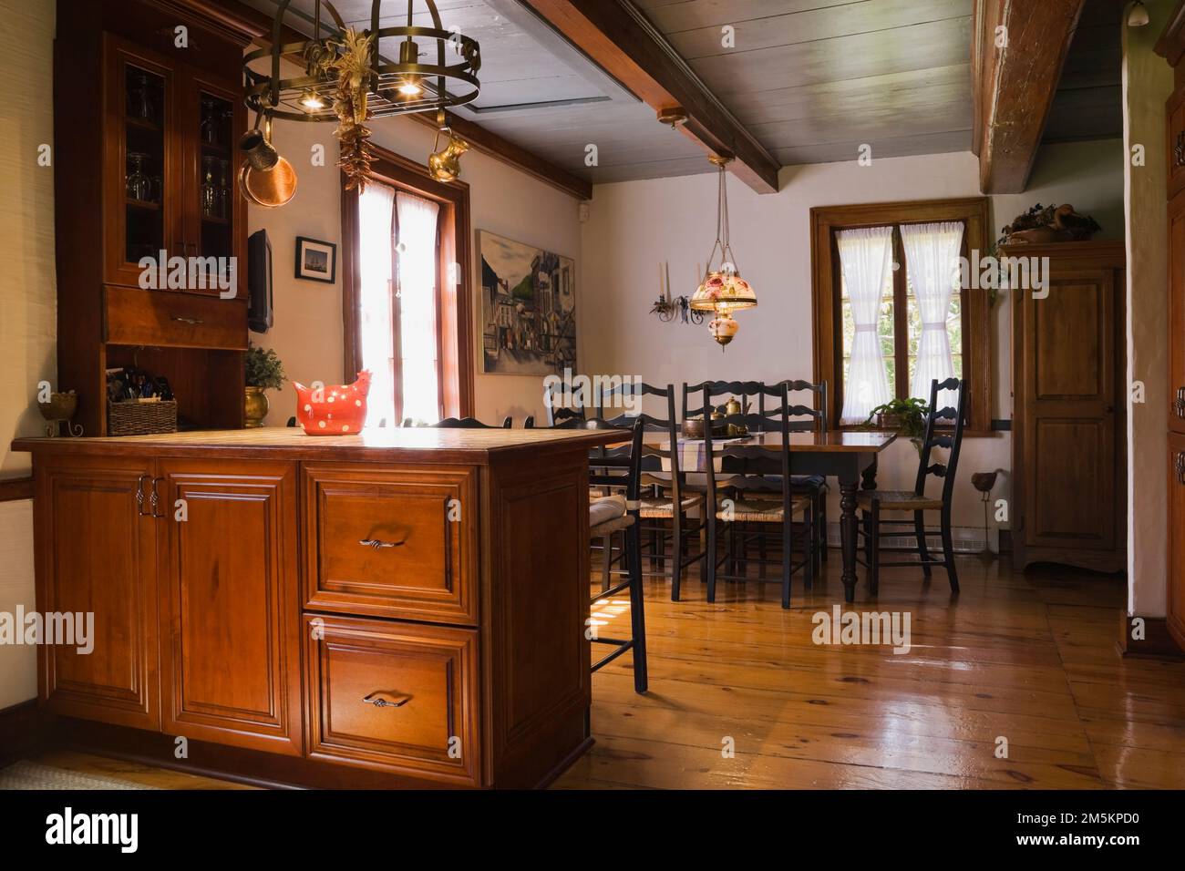 Isola con piano in ceramica Tan e tavolo da pranzo in legno antico con sedie a sedere in tessuto con schienale alto nella sala da pranzo all'interno di una casa di legno ricostruita degli anni '1840. Foto Stock