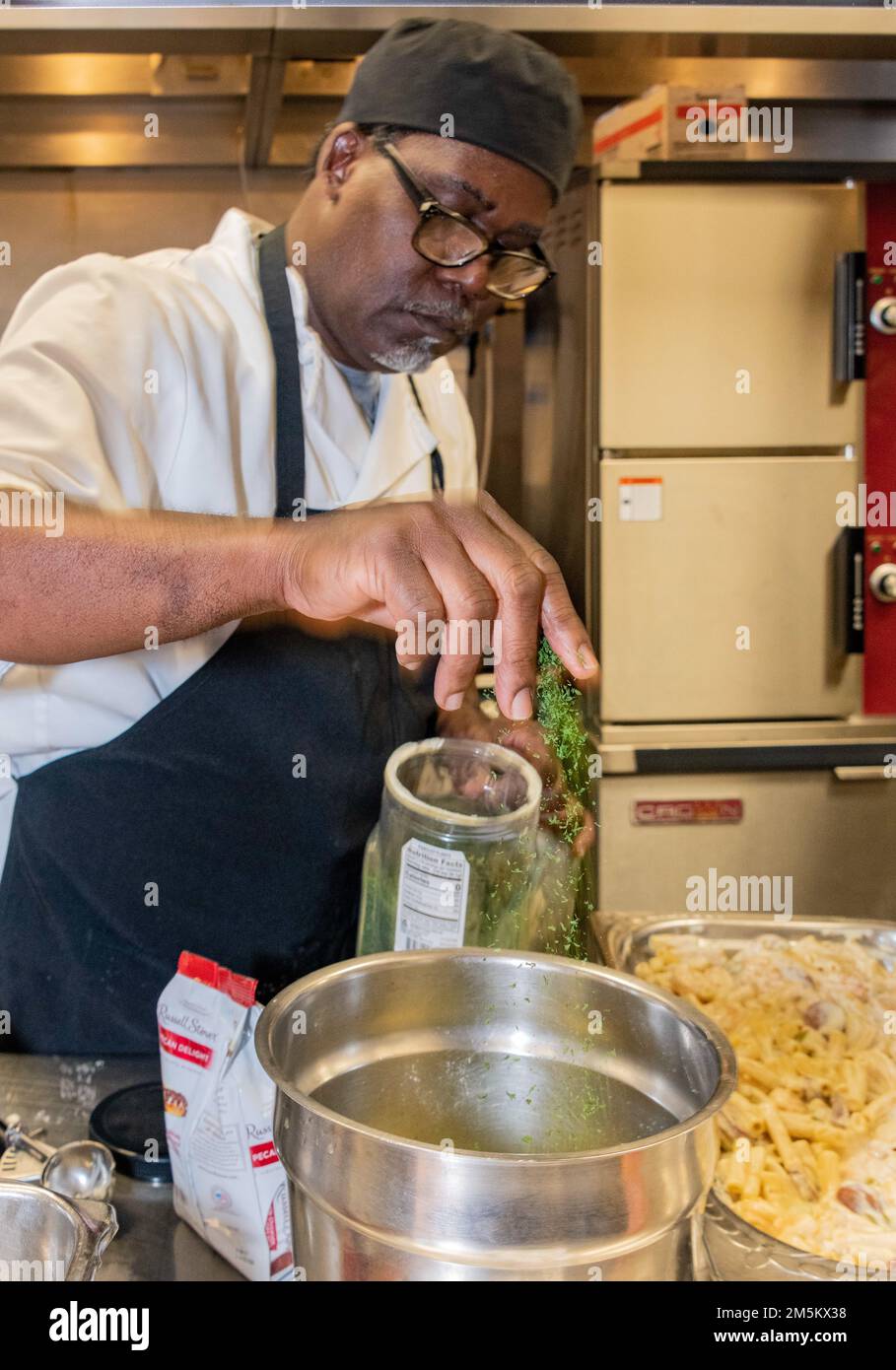 Reginald Barkus, 60th Force Support Squadron food Service Cook, aggiunge prezzemolo a una ciotola di miscelazione presso Travis Air Force base, California, 23 marzo 2022. Il 60th Mission Support Group Monarch Dining Facility ha ospitato un concorso di cucina che mostra abilità, velocità e ingegnosità. Squadre di quattro persone si sono esibite per trasformare gli ingredienti misteriosi in piatti di portata principale e dessert da presentare a un gruppo di giudici. Foto Stock