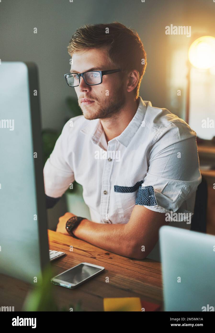 Mettere nelle ore. un giovane designer che lavora su un computer mentre  indossa gli occhiali in ufficio Foto stock - Alamy