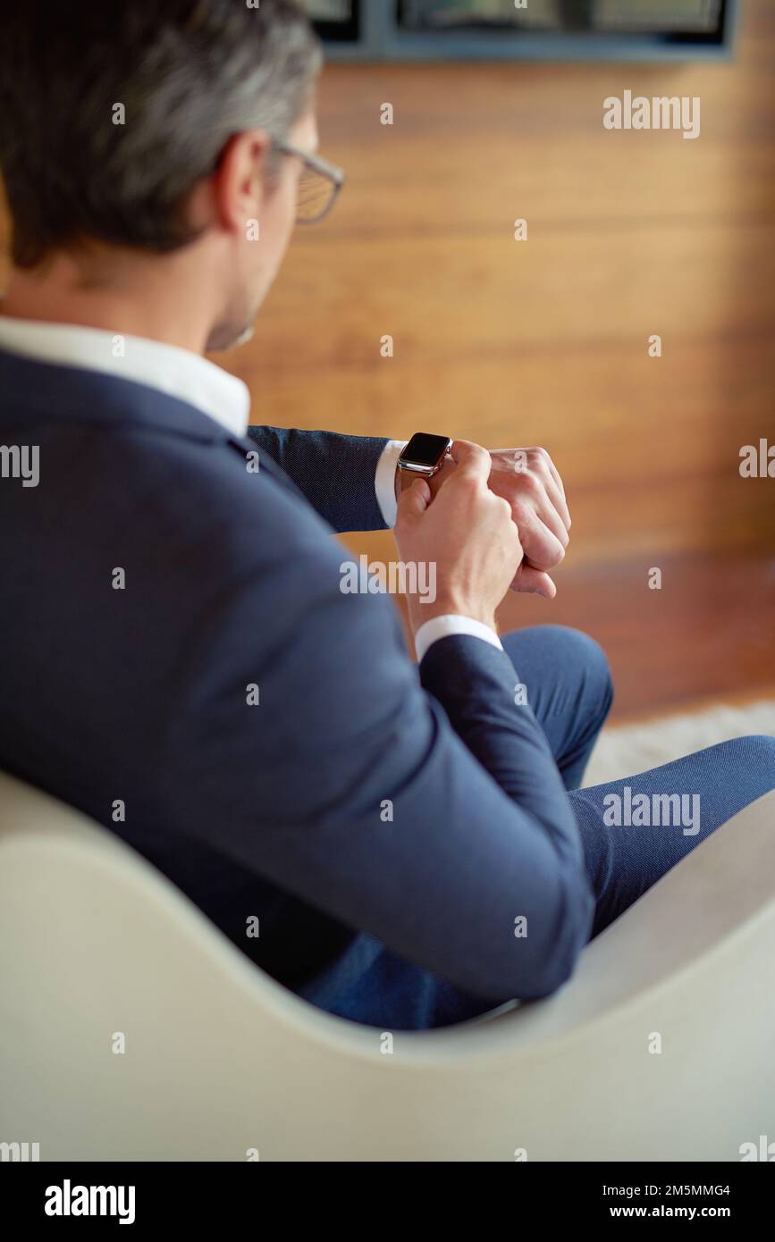 Il business si basa su una buona gestione del tempo. un uomo d'affari che controlla il suo orologio mentre è seduto in un ufficio aziendale. Foto Stock