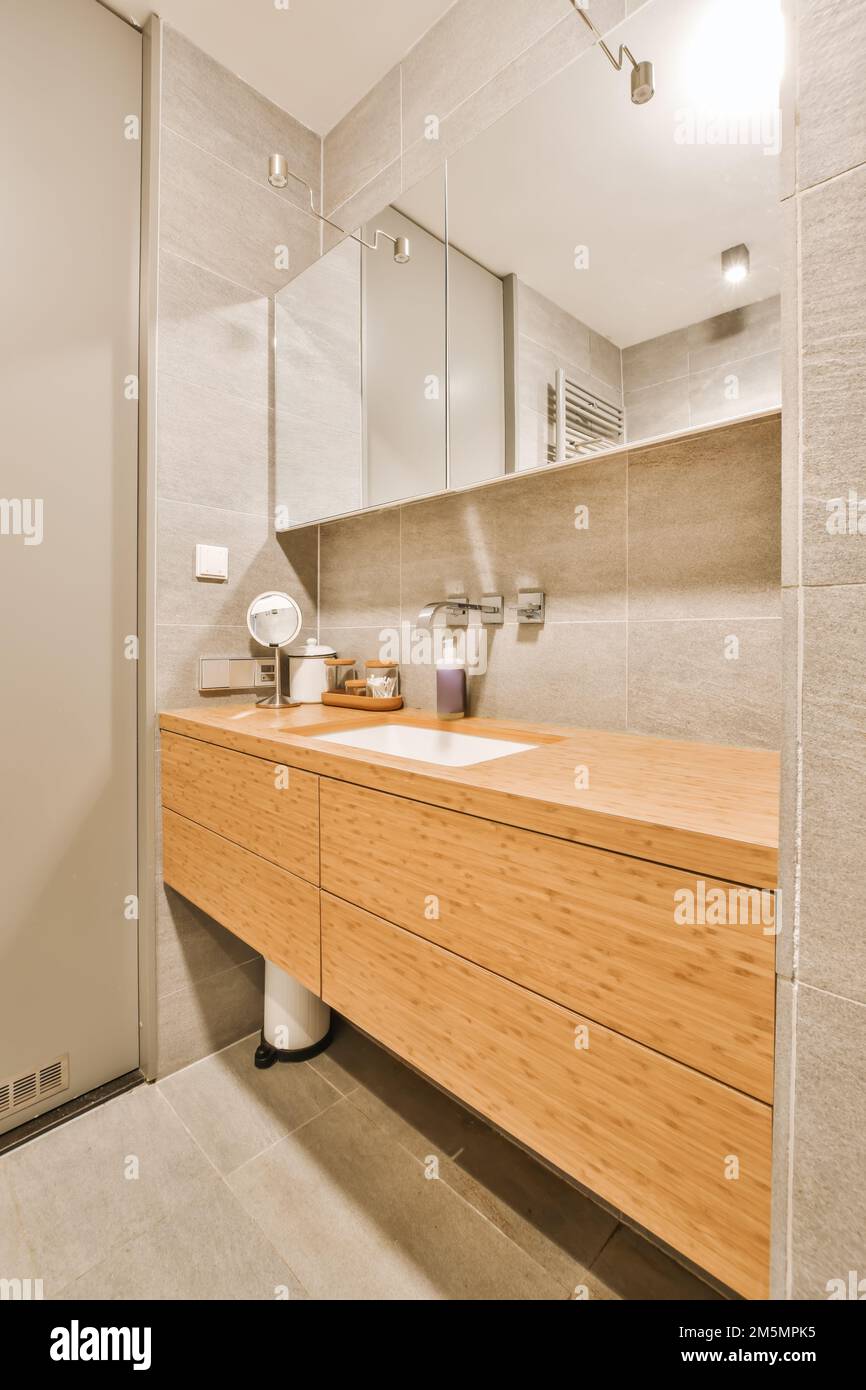 un bagno moderno con armadietti in legno e specchi alle pareti, unitamente ad un toilet bianca nell'angolo accanto al lavandino Foto Stock