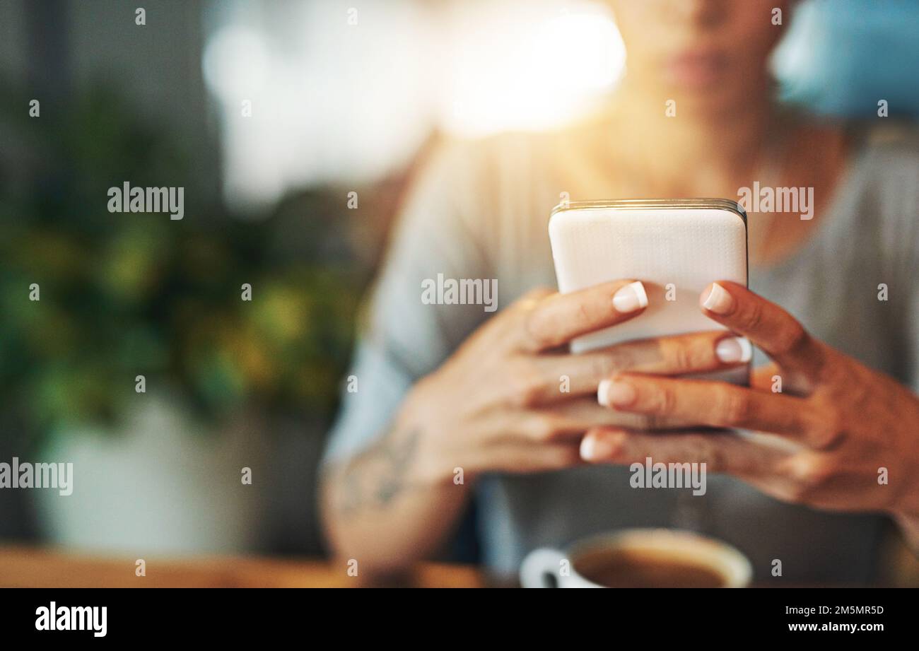 Invio di un aggiornamento SMS. una giovane donna che invia un sms mentre lavora tardi nel suo ufficio. Foto Stock