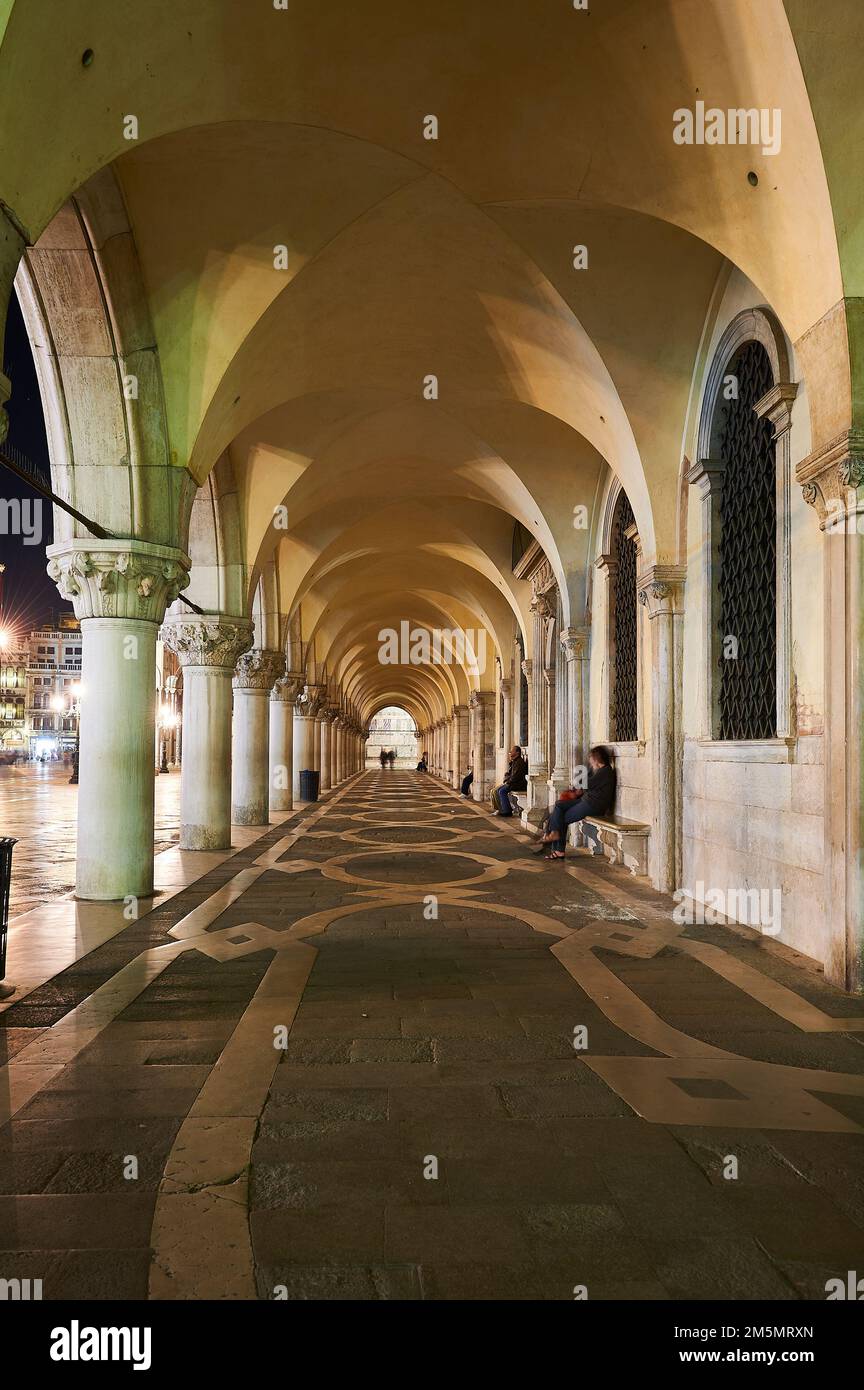 La gente seduta in appoggio sotto gli archi di Piazza San Marco a Venezia, Italia Foto Stock