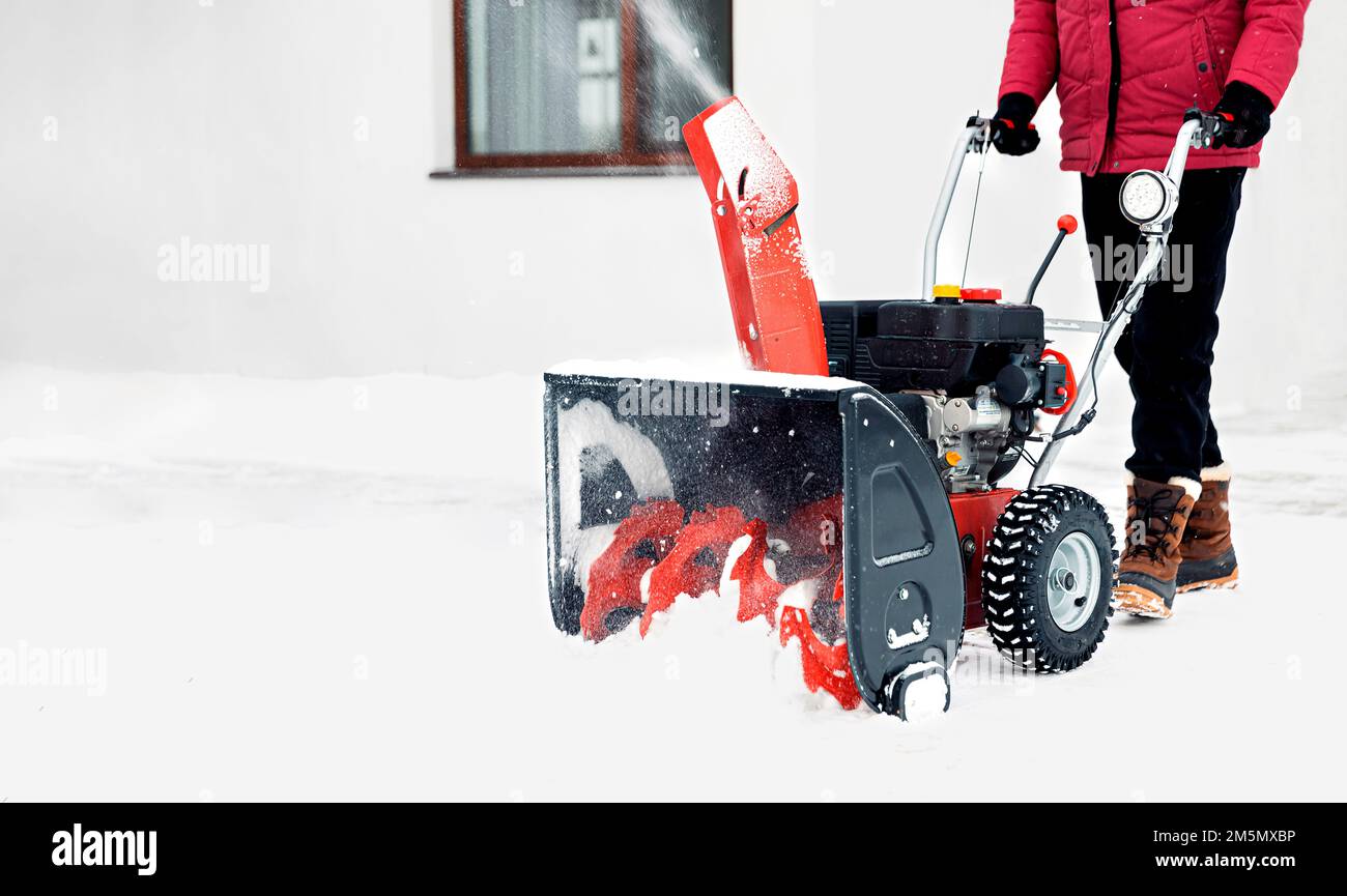 Spazzaneve alimentato a benzina in azione. Uomo all'aperto di fronte a casa con una fresa da neve. Rimozione della neve, assistente lanciatore in inverno fuori casa. Giovane lavoratore che soffia neve durante la Blizzard Foto Stock