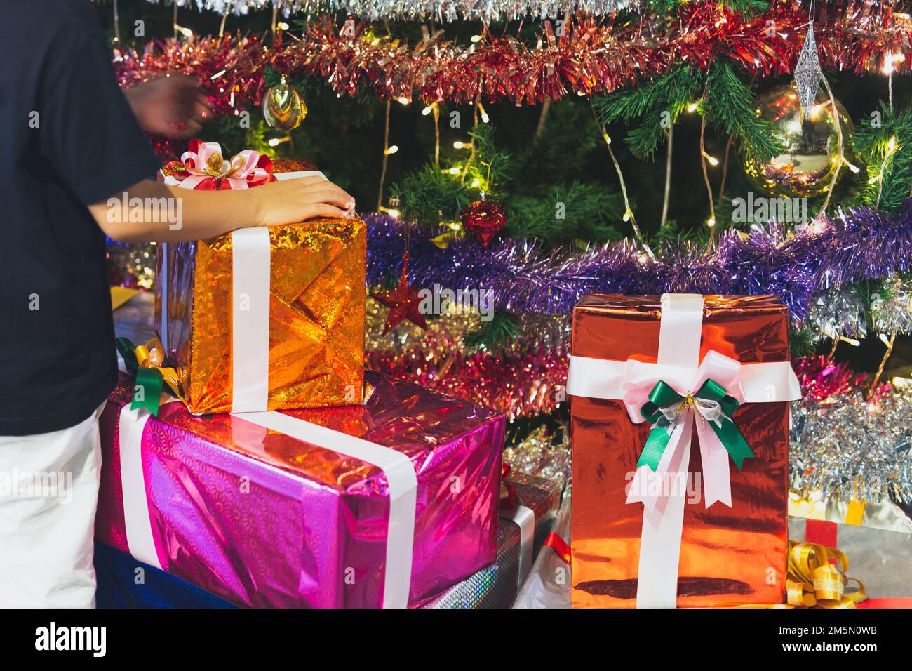 Mano dei bambini sui regali di natale e sulle scatole del regalo sotto l'albero di Natale Foto Stock