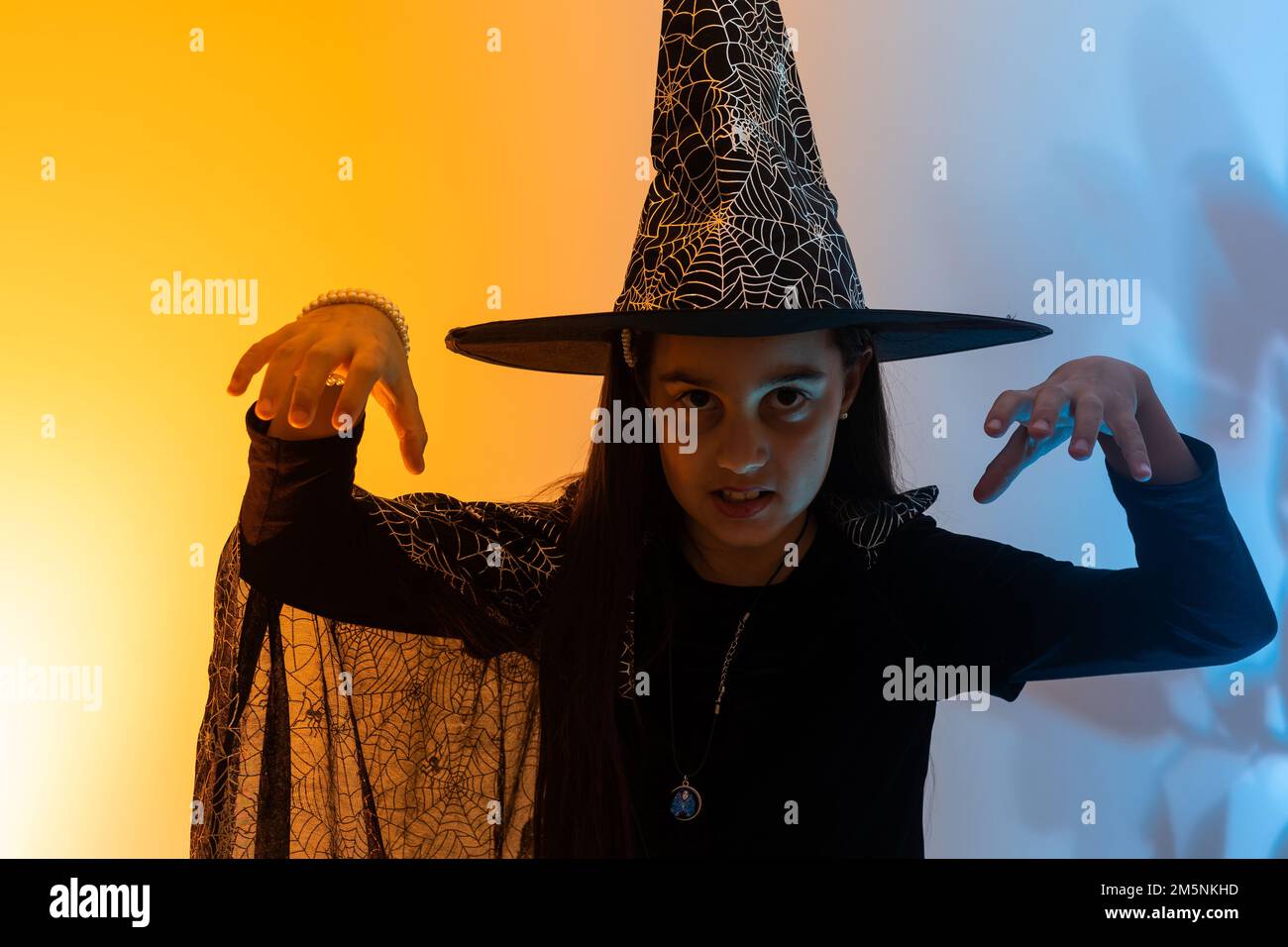 Una strega giovane e graziosa. Festa di Halloween. Ritratto di una ragazza adolescente carina in posa in studio in costume di una strega e una bacchetta magica in mano. Misto Foto Stock