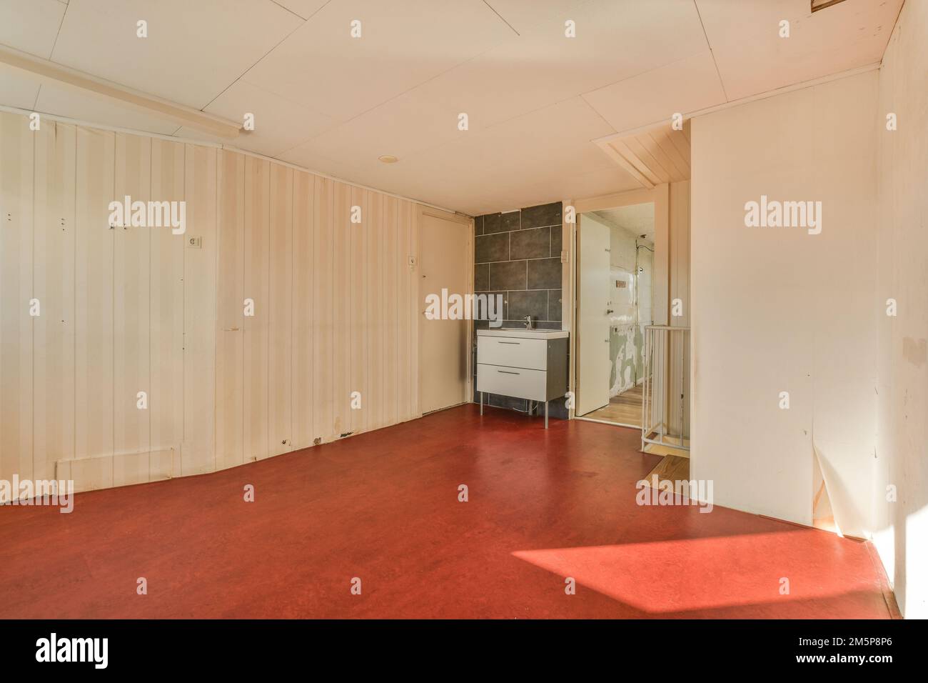 una stanza vuota con pavimento rosso e sfondi bianchi alle pareti, di fronte ad uno specchio Foto Stock