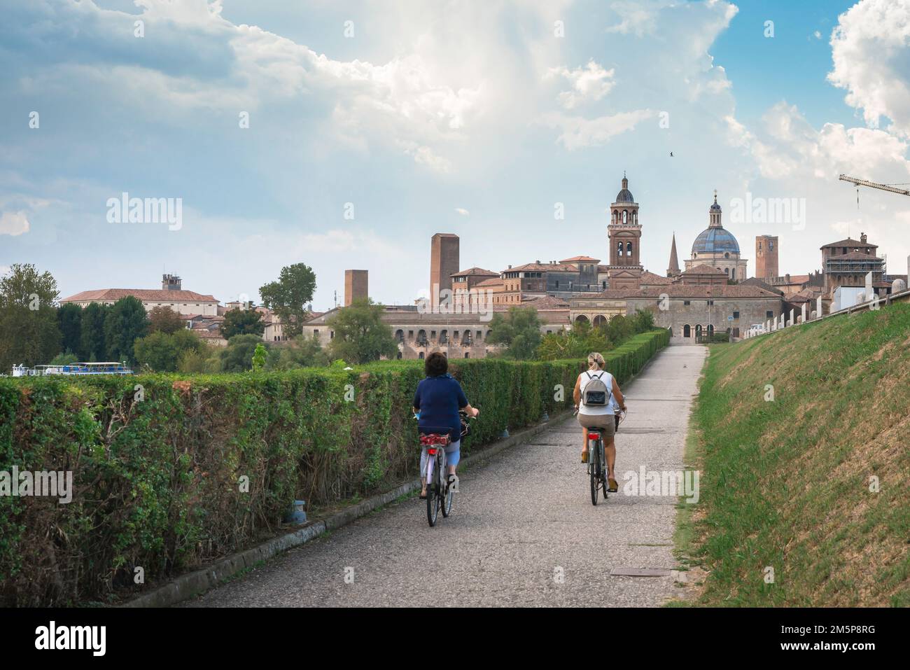 Ciclismo Italia, vista posteriore in estate di due donne in bicicletta verso la panoramica città rinascimentale di Mantova (Mantova) in Lombardia Foto Stock