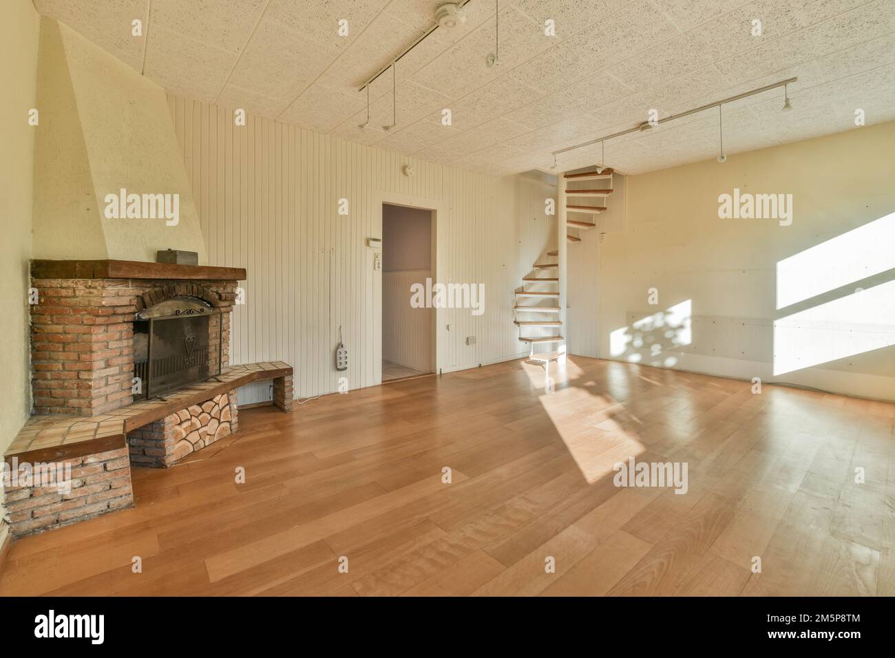 un soggiorno vuoto con pavimenti in legno e un camino in mattoni in camera è molto pulito, ma è difficile da vedere Foto Stock