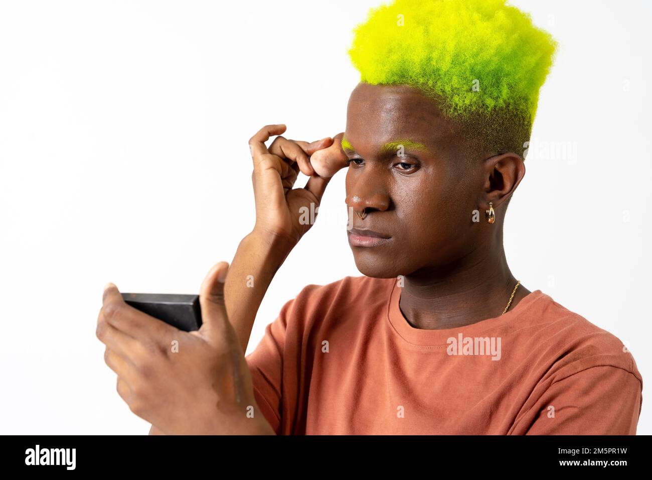 Un maschio afro-spagnolo con capelli verdi che mettono il trucco sul suo viso Foto Stock