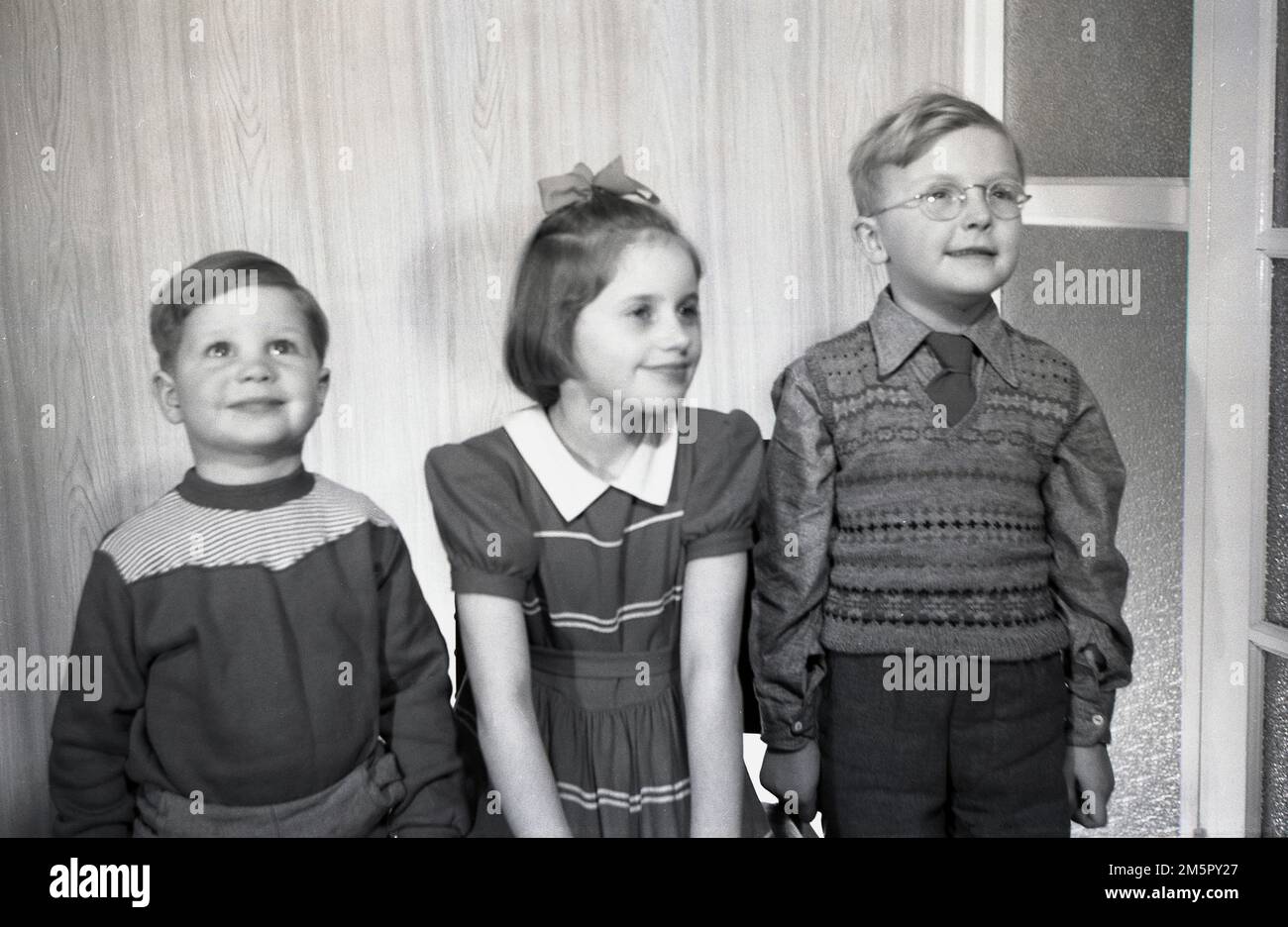 Anni '1950, storici, al chiuso, tre bambini stanno per scattare foto nei vestiti dell'epoca, il ragazzino che indossa una canotta senza maniche e la bambina con un fiocco di capelli, Inghilterra, Regno Unito. Foto Stock