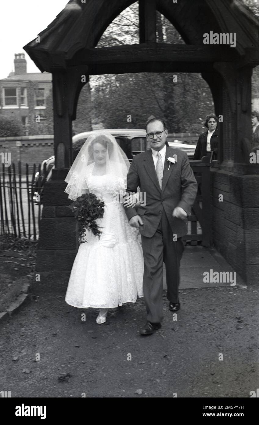 1950, storica, una sposa accompagnata da suo padre che cammina lungo il sentiero all'ingresso esterno della chiesa, Inghilterra, Regno Unito. Foto Stock