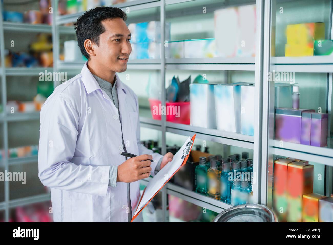 farmacista asiatico in penna di tenuta uniforme e oggetti di controllo per appunti Foto Stock