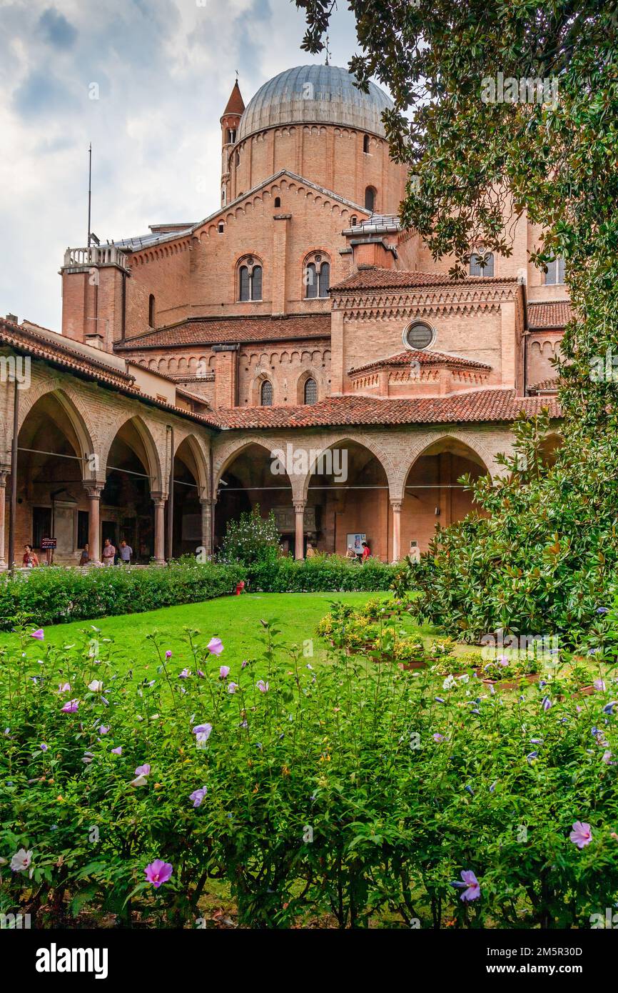Basilica di Sant'Antonio vista dal Chiostro della Magnolia a Padova, le sue cupole in mattoni che si innalzano sopra archi gotici e un giardino fiorito. Foto Stock