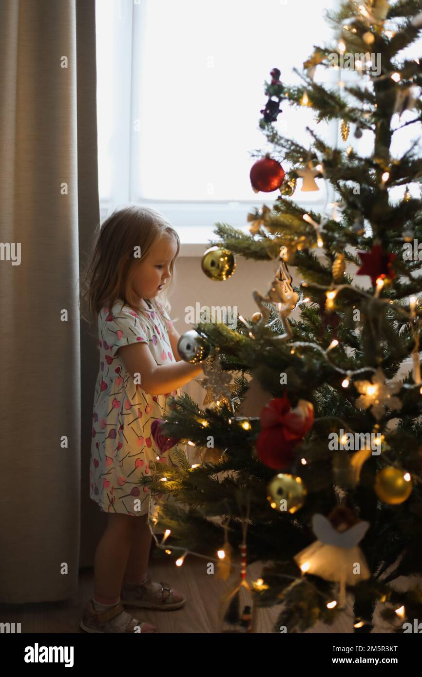 Bambina la decorazione di albero di Natale con i giocattoli e baubles. Carino kid preparare a casa per la celebrazione del Natale. Foto Stock