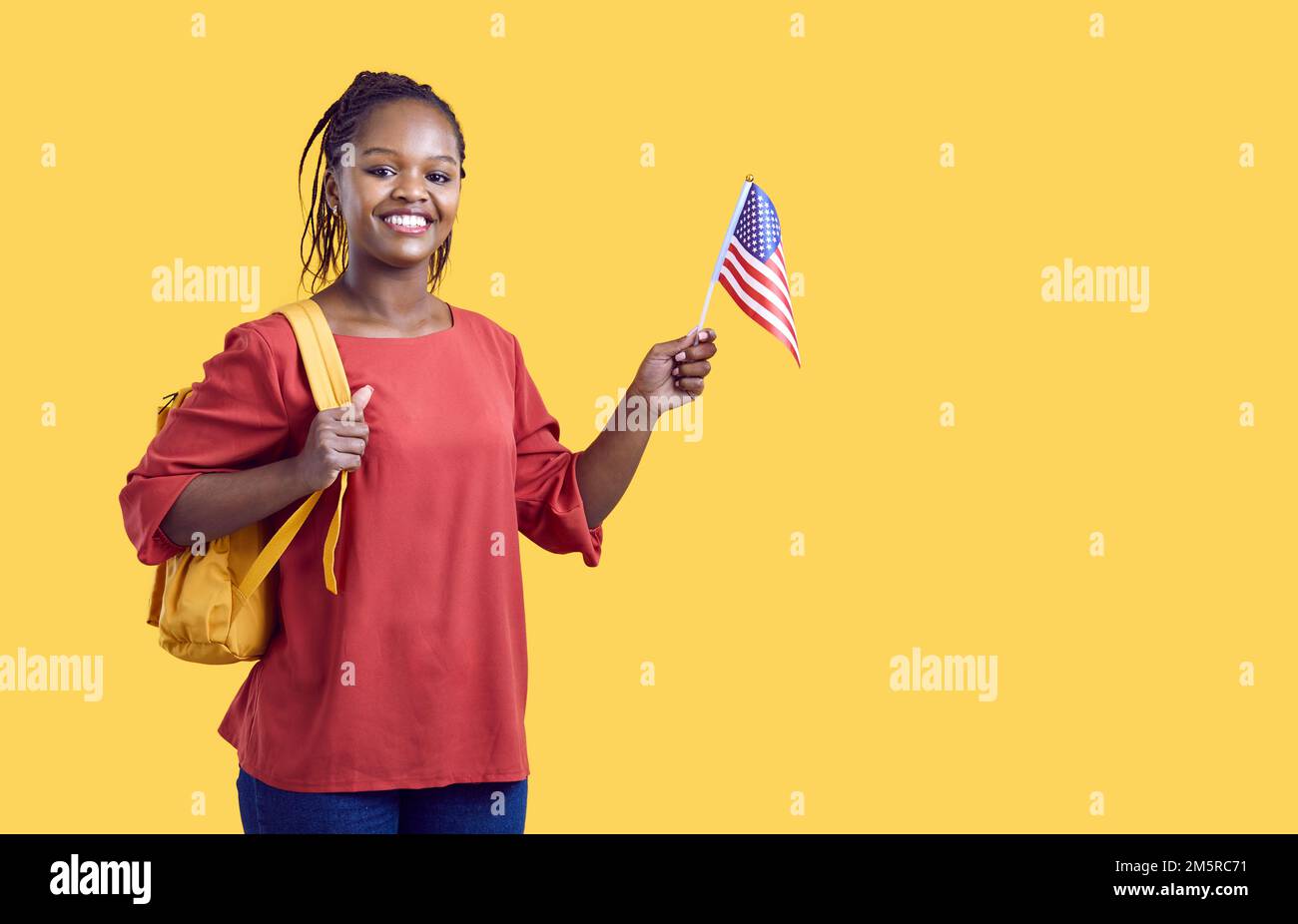 Felice studente nero universitario in piedi sullo sfondo dello spazio copia, tenendo la bandiera americana e sorridendo Foto Stock