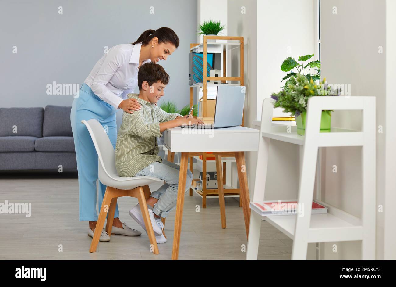 Madre che aiuta un figlio che è seduto alla scrivania con un computer portatile e che fa i compiti a casa nel suo notebook Foto Stock