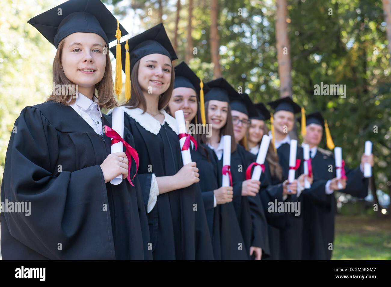 Fila di giovani in abiti da laurea all'aperto. Età studente. Foto Stock