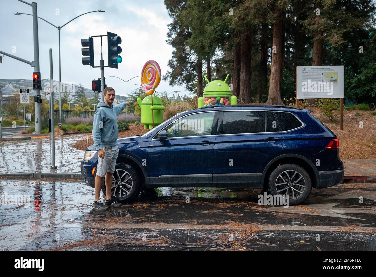 Uomo che mostra le statue di google android in giardino in piedi in auto su strada bagnata Foto Stock