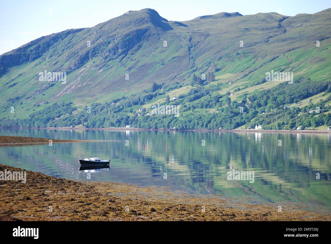 La vista da Leckmelm attraverso Loch Broom a Letters & Ardindrean sulla riva lontana, nr Ullapool in Scozia. Una barca per il tempo libero è ormeggiata in primo piano Foto Stock